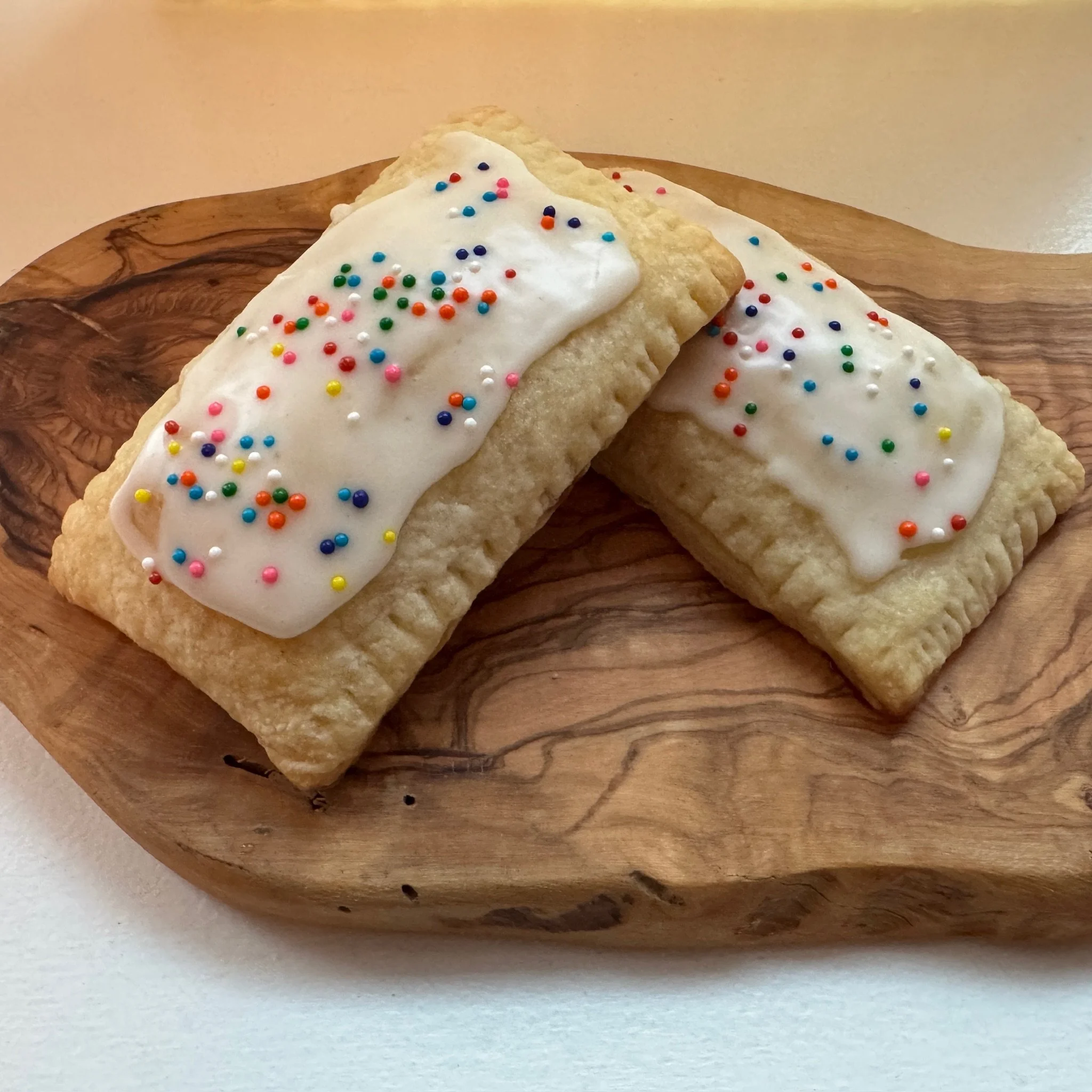 Pop tarts with white frosting and colorful sprinkles on a wooden plate.