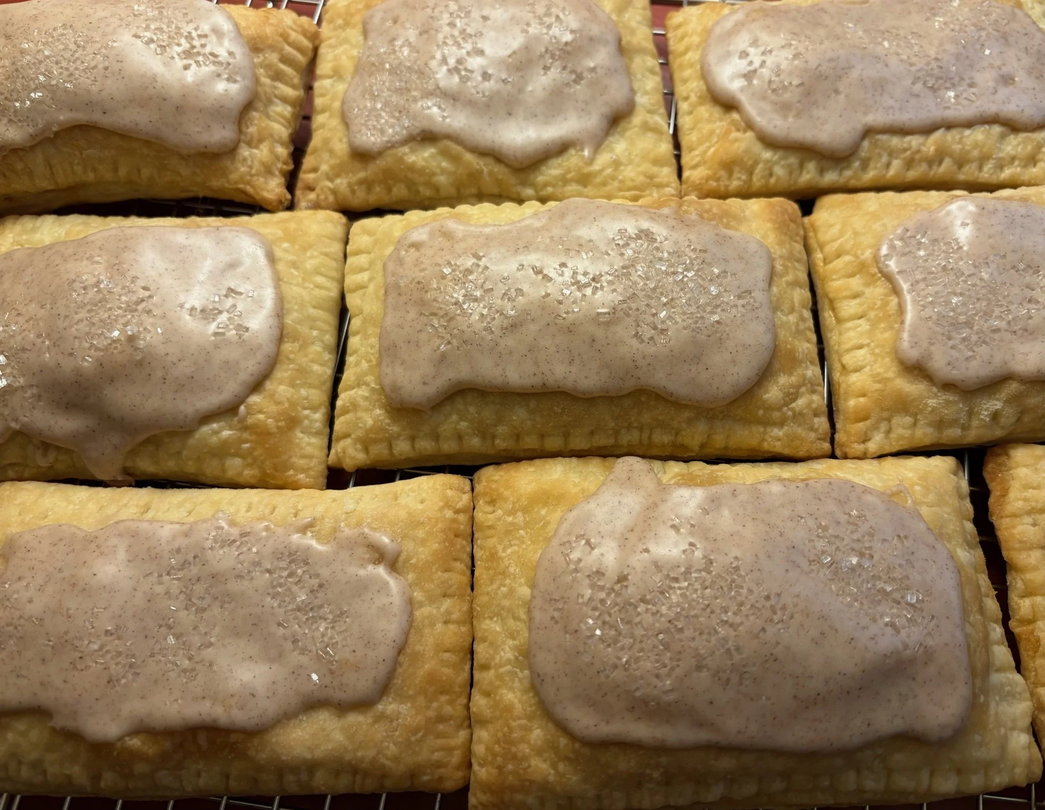Close-up of six rectangular brown sugar cinnamon pastry squares with a light-colored glaze on top, sprinkled with sugar, arranged on a wire rack.