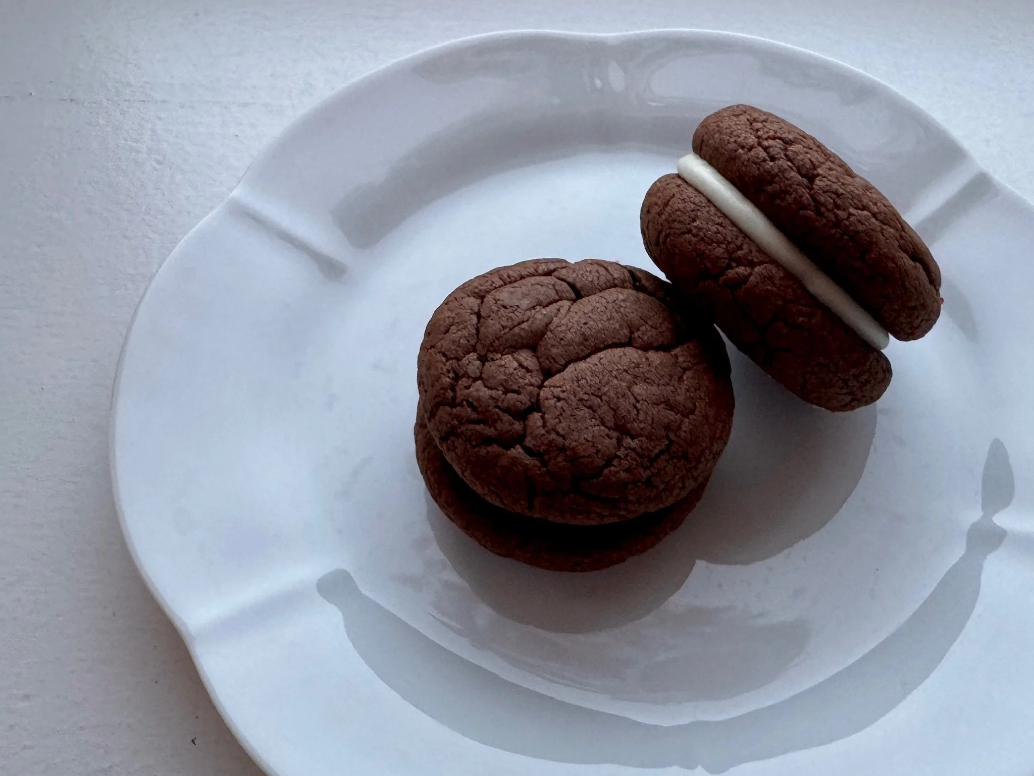 Two chocolate cookies with white cream filling on a white plate.