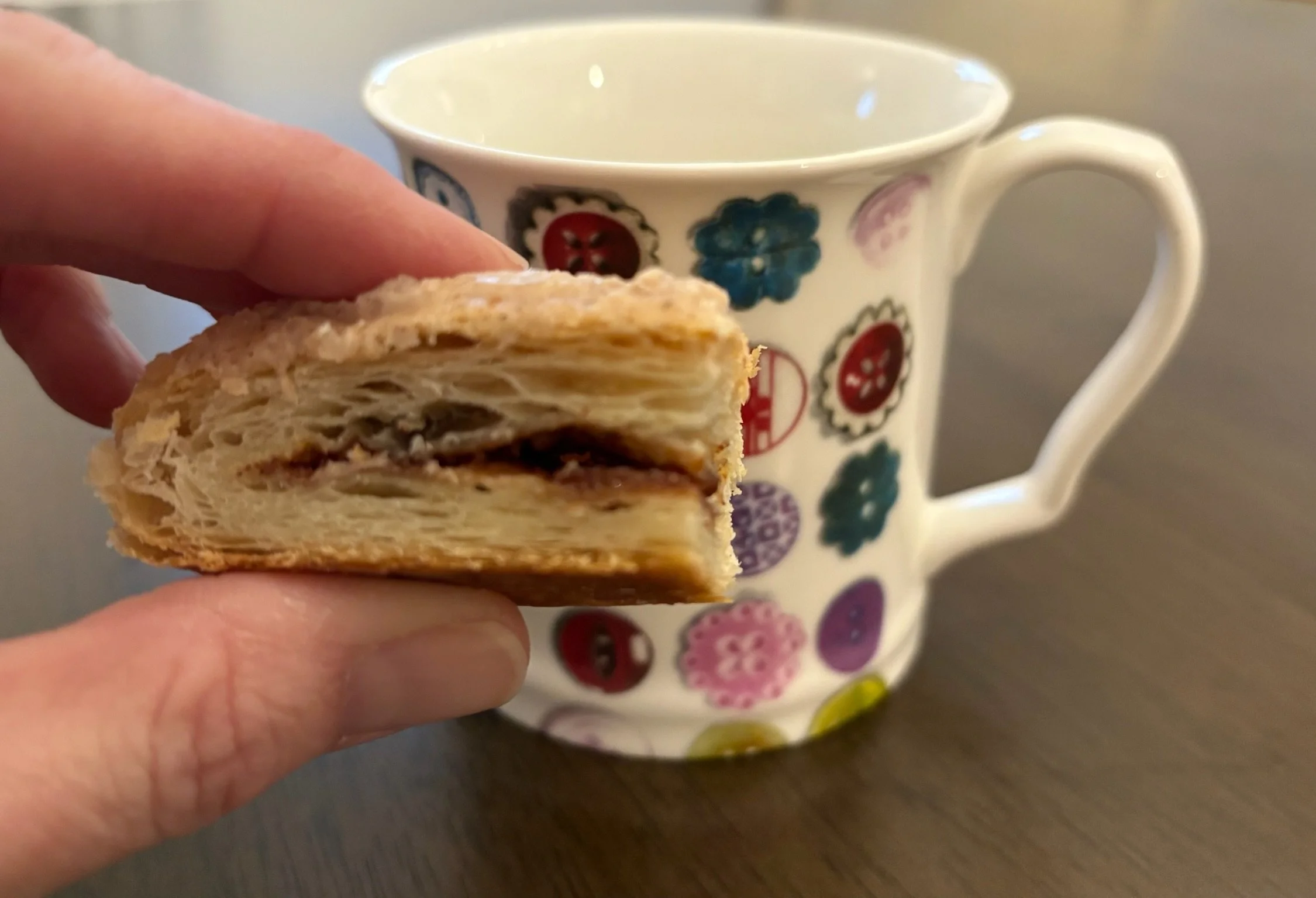 A person holding a layered pastry with a filling in front of a colorful decorated mug.