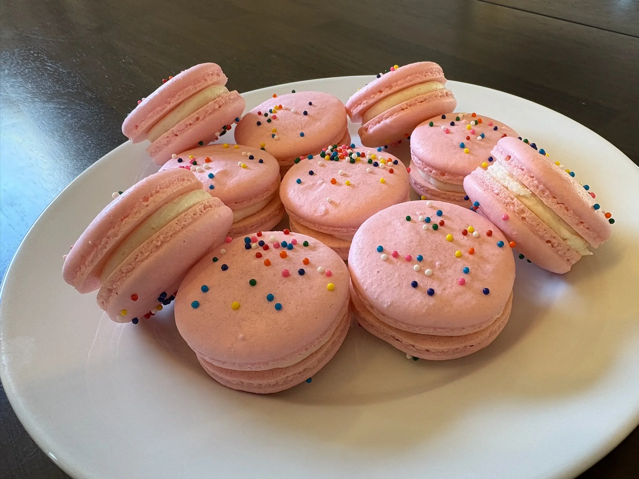 A white plate filled with pink macarons topped with colorful sprinkles.