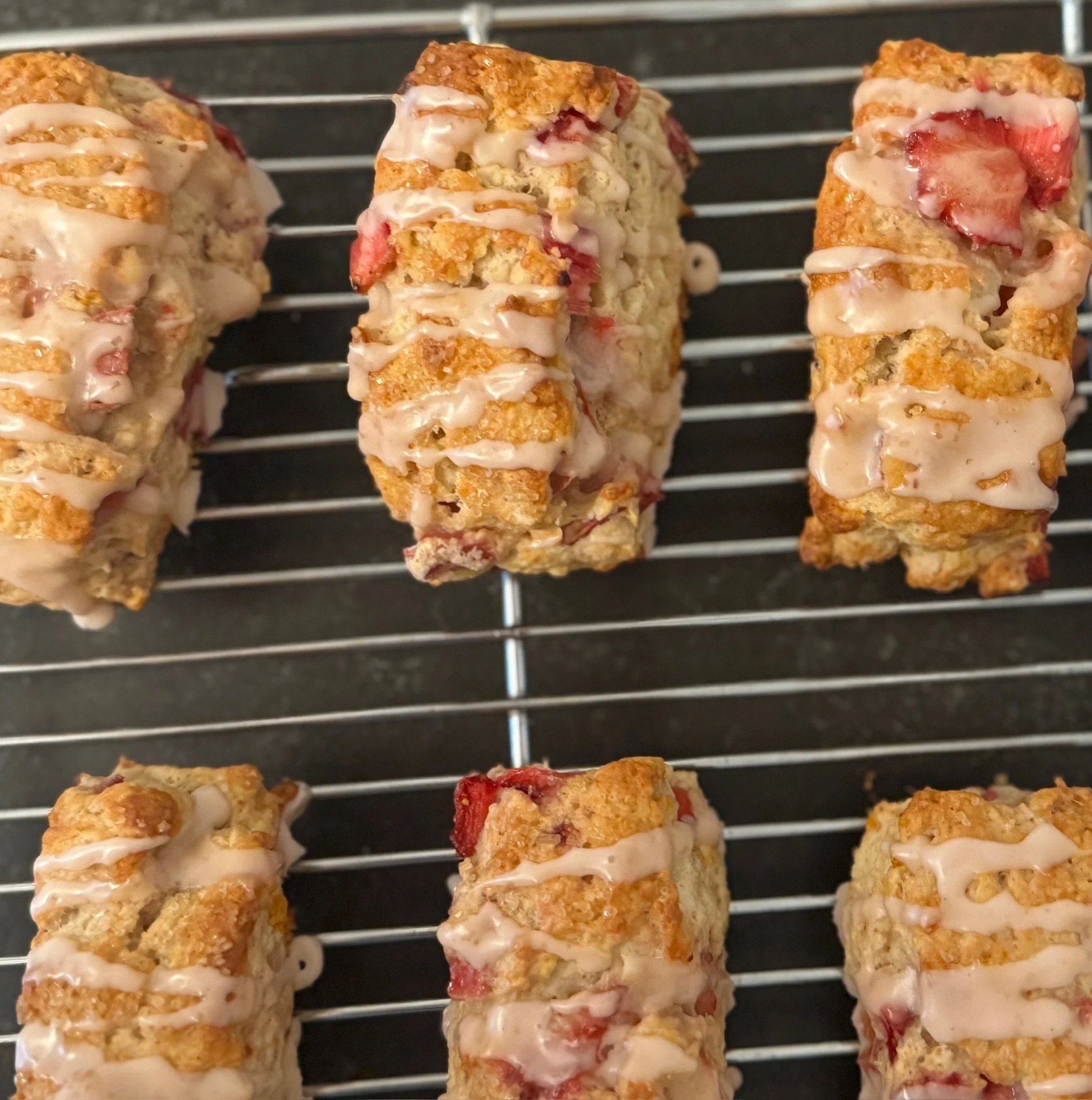 Several strawberries and possibly cream or yogurt between layered biscuit cookies on a wire rack.