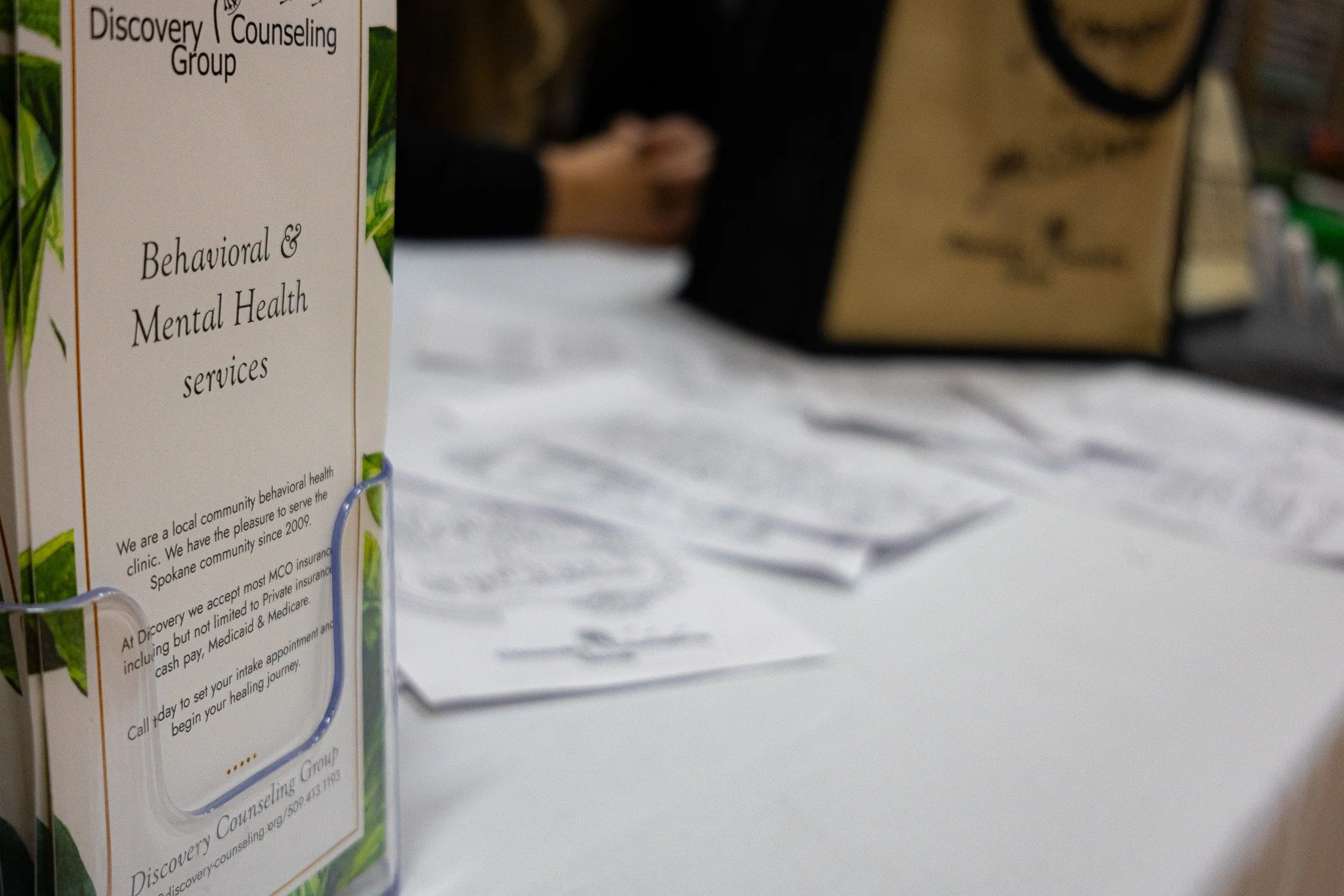 A pamphlet for a community mental health services discovery and counseling group, with blurry hands and a bag in the background on a table.