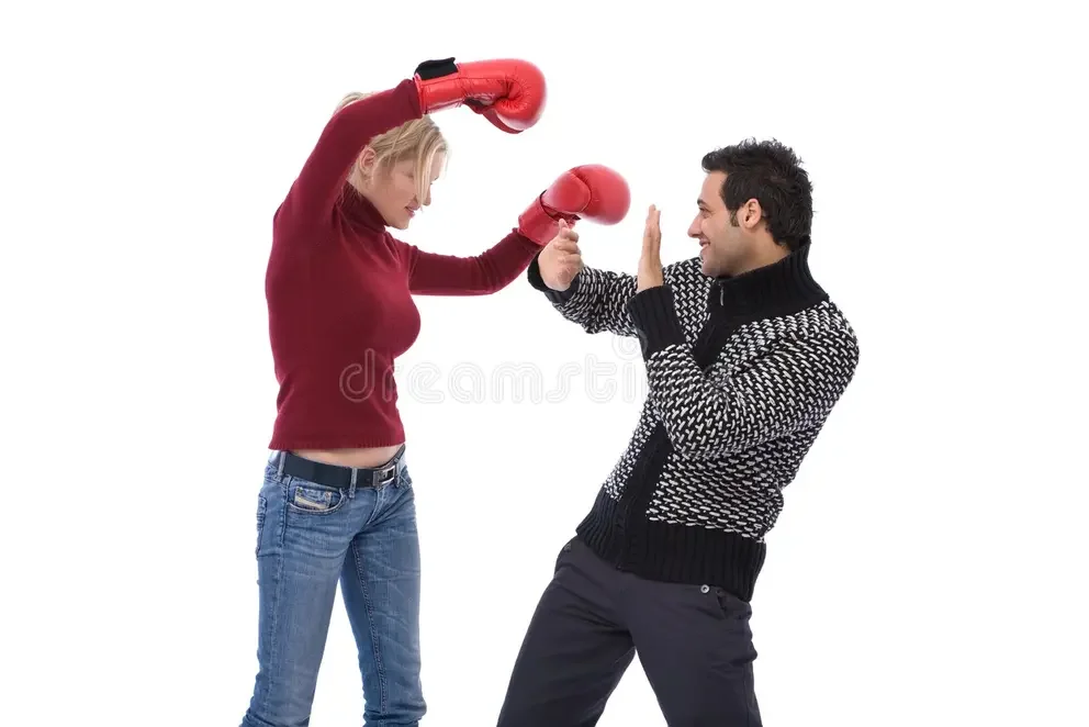 A woman in a red sweater and jeans wearing boxing gloves sparring with a man in a black and white sweater who is defending.