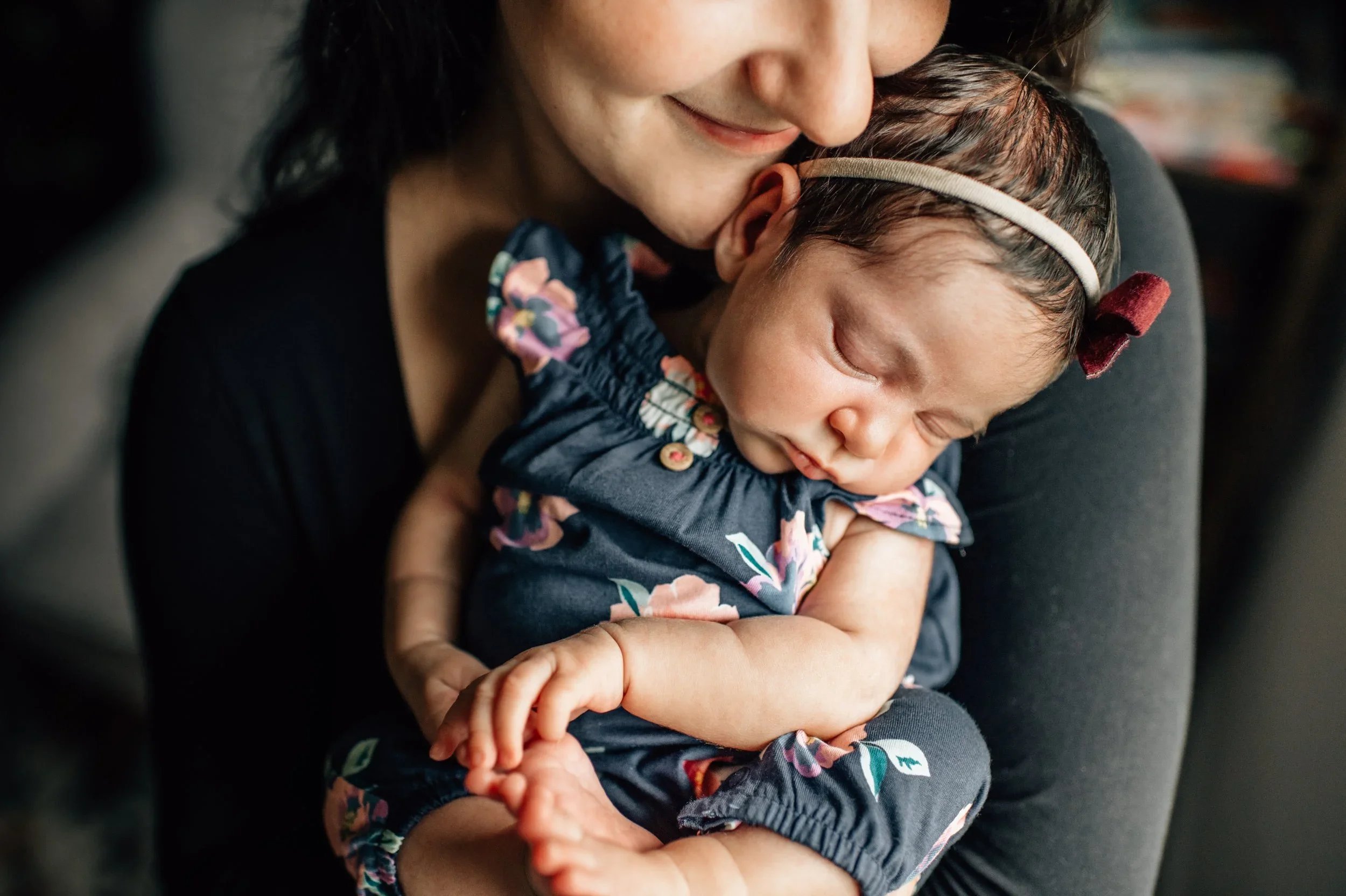 A woman holding a sleeping baby close to her chest, both with peaceful expressions, in a cozy indoor setting.