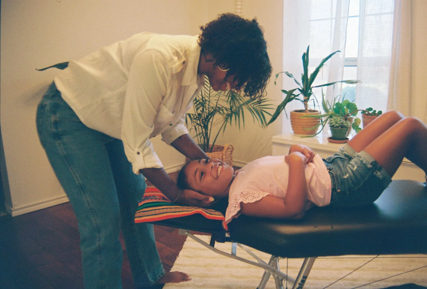 A kid lying down, smiling while a chiropractor holds her head gently, giving her an adjustment.