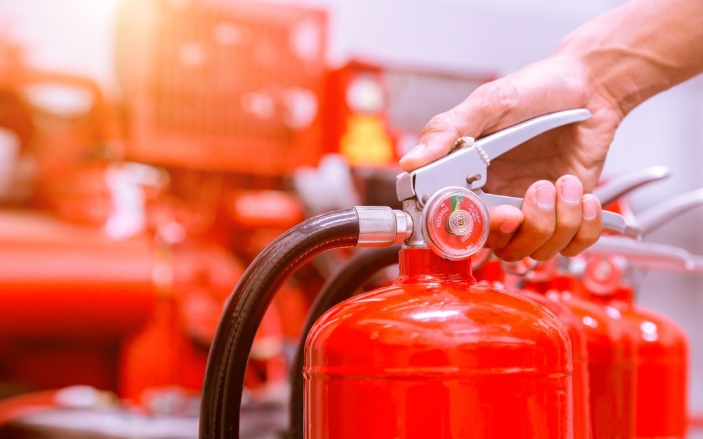 A person preparing to use a fire extinguisher during a fire safety demonstration, with multiple fire extinguishers in the background.