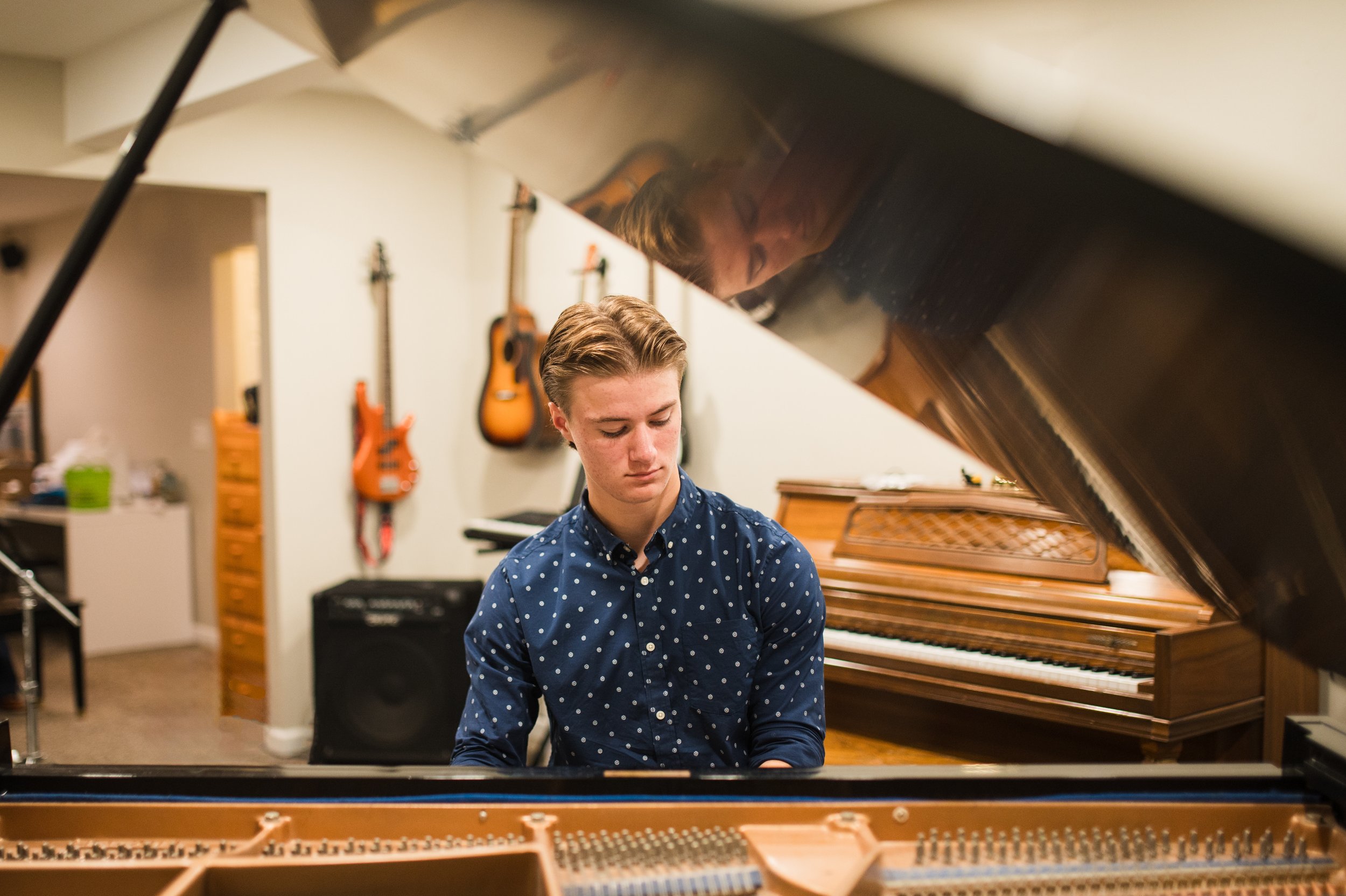 Young man playing the piano in a music studio with guitars hanging on the wall in the background.