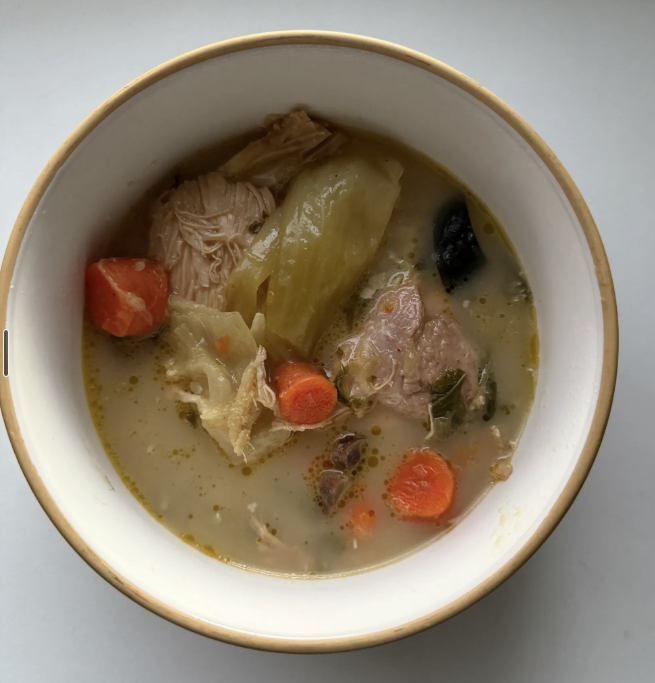 A bowl of chicken vegetable soup with carrots, celery, black olives, and shredded chicken.