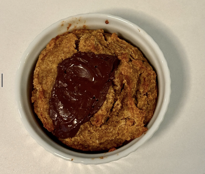 Chocolate chip cookie with a dollop of melted chocolate on top, in a white ramekin on a white surface.