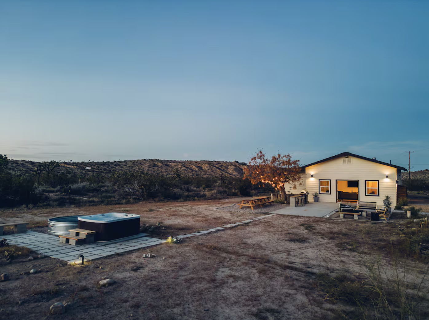 Tiny house with outdoor seating area and hot tub in a desert landscape during twilight.