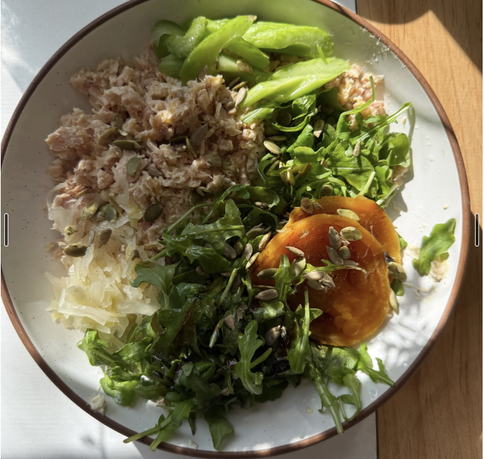 Plate with mixed greens, shredded carrots, shredded cheese, tuna salad, and sliced cucumber.