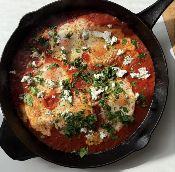 Cast iron skillet containing eggs in tomato sauce topped with crumbled cheese and chopped fresh herbs.