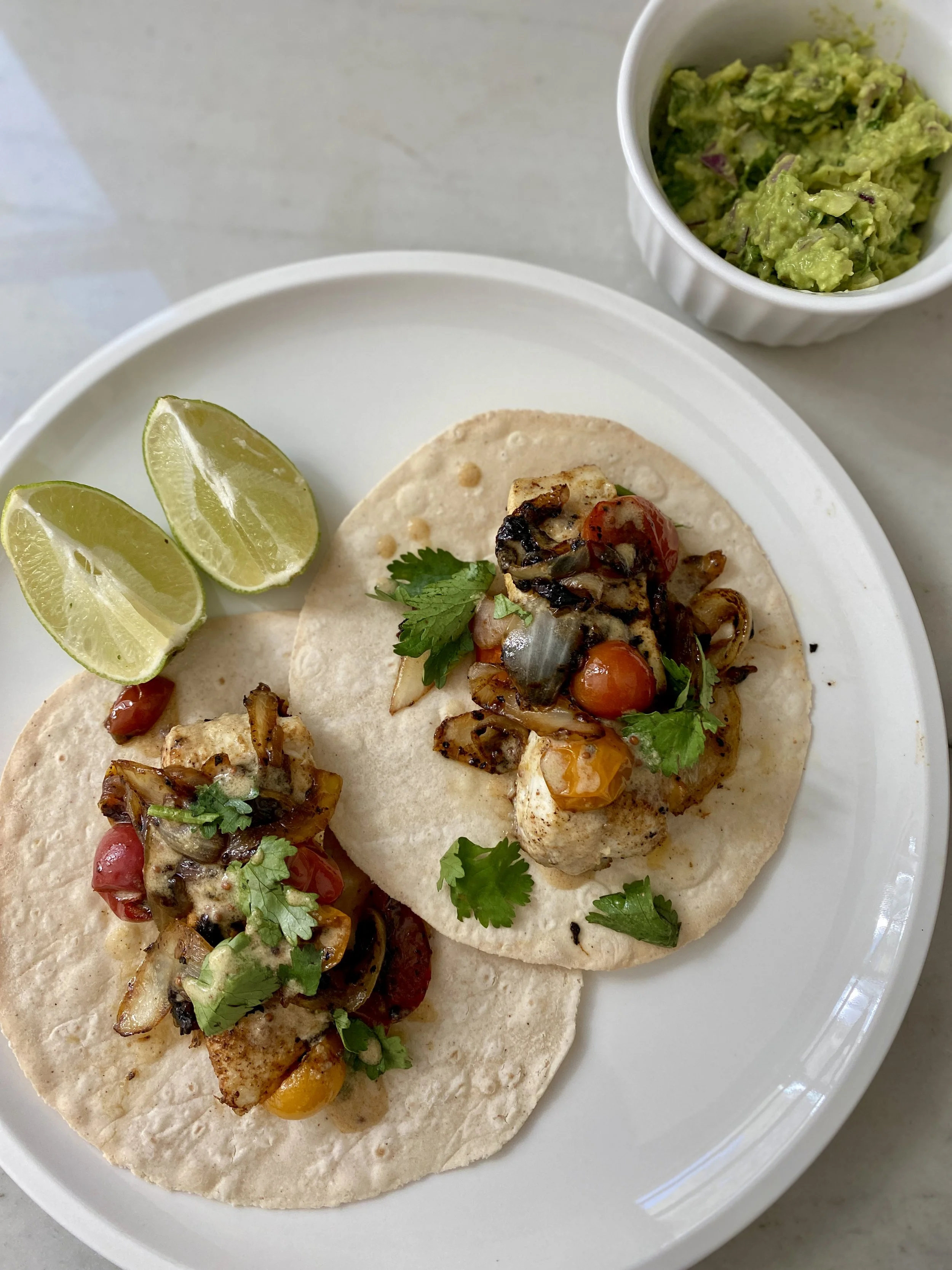 Three street tacos on a white plate with lime wedges and a side of guacamole.