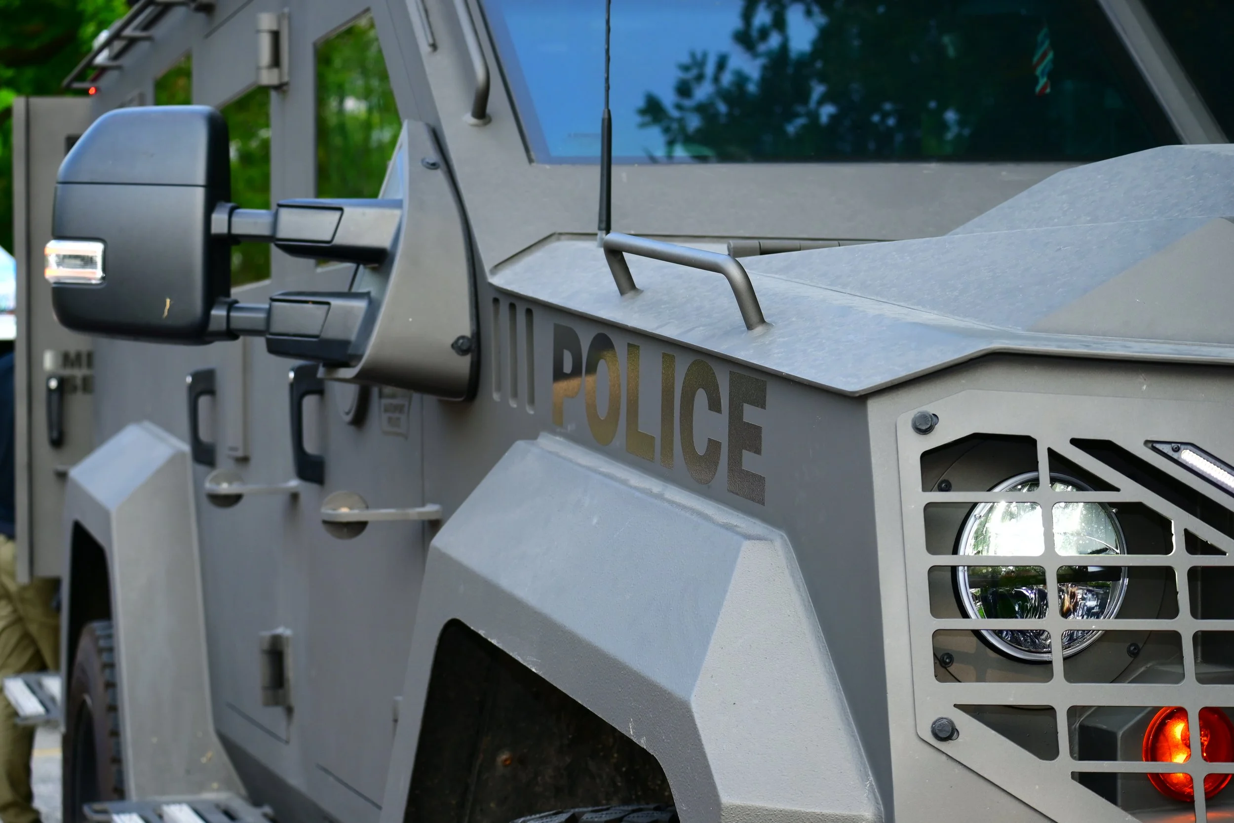 A close-up of a tactical police vehicle with the word "POLICE" partially visible, featuring metal and plastic components, side mirrors, and rear lights.