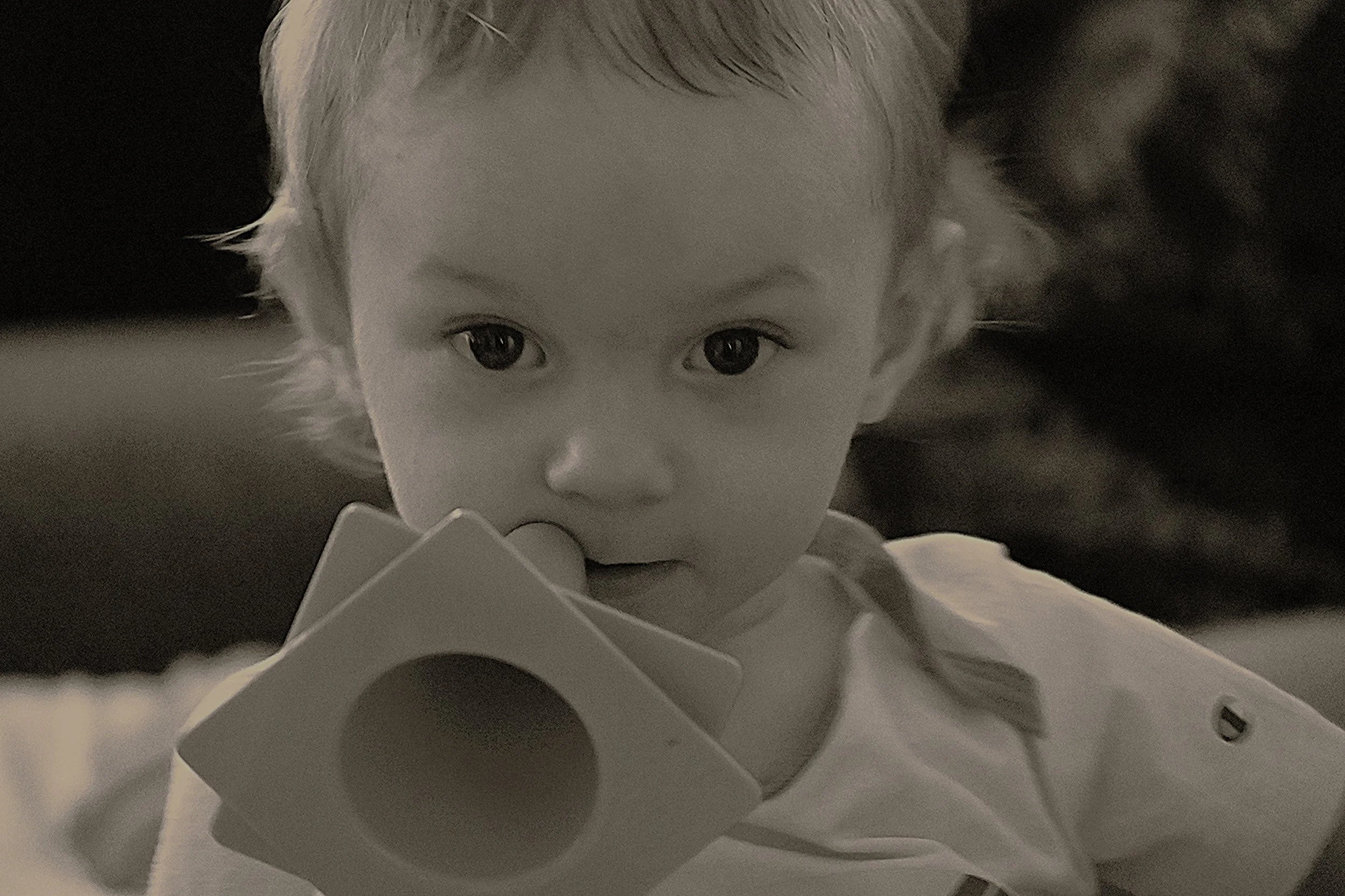 A young child with light hair looking directly at the camera, resting their chin on a surface with a soft focused background.