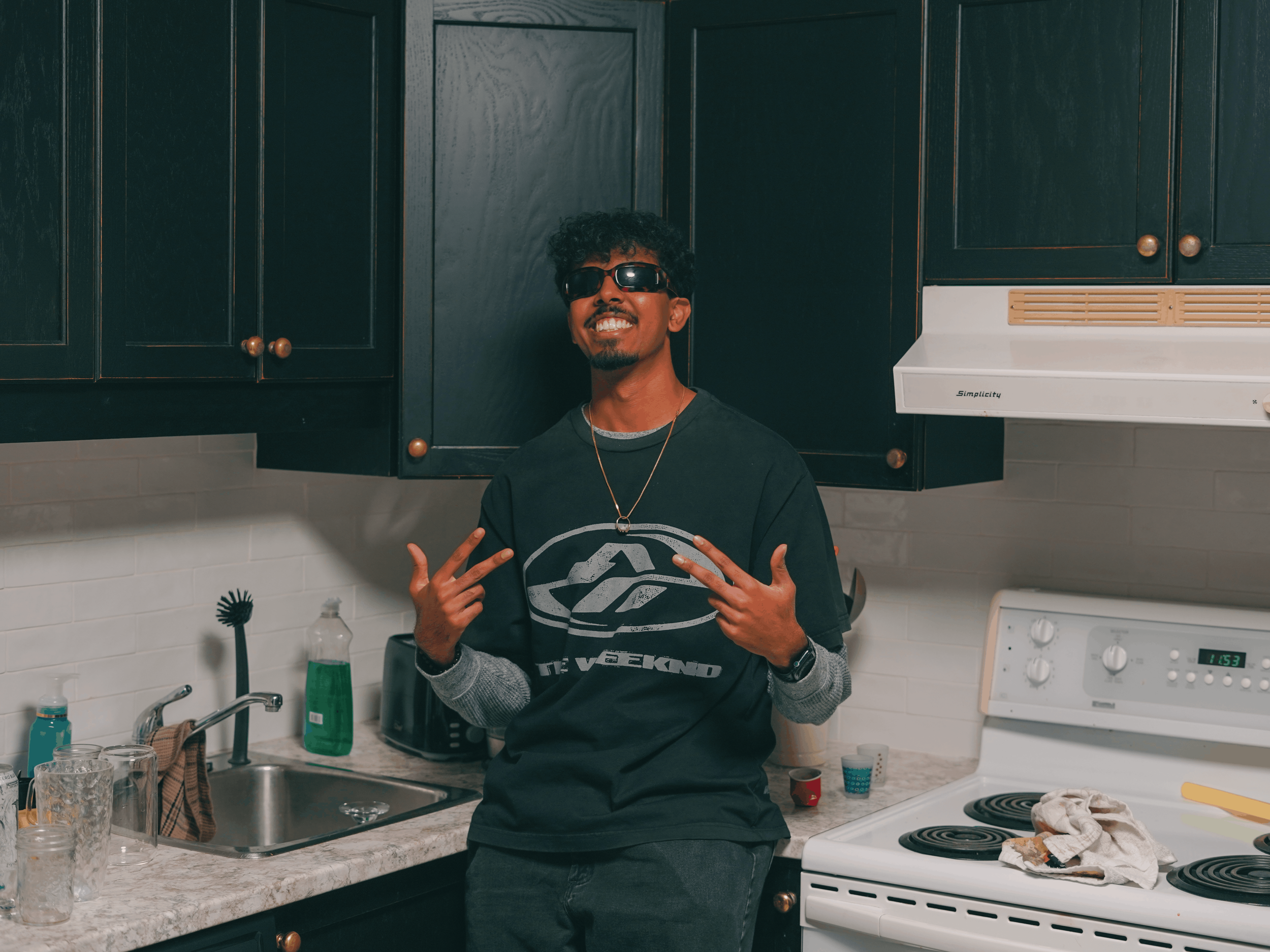 A photo of Addy, the founder of Valence Auto Detailing. He is a man with curly hair, sunglasses, and a black shirt making peace signs with both hands.