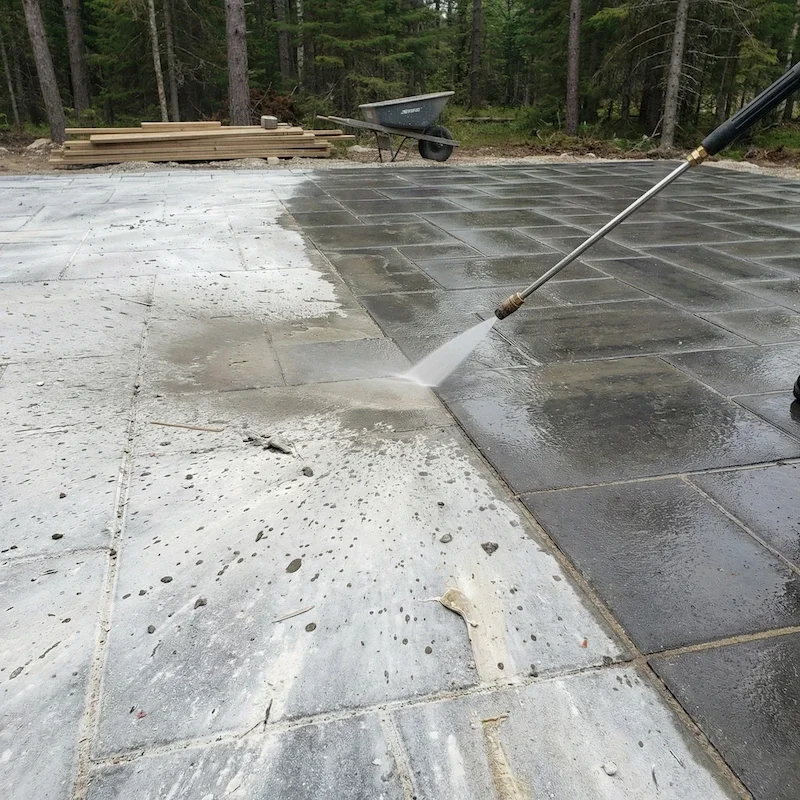 A pressure washer cleaning driveway pavers in a wooded outdoor area