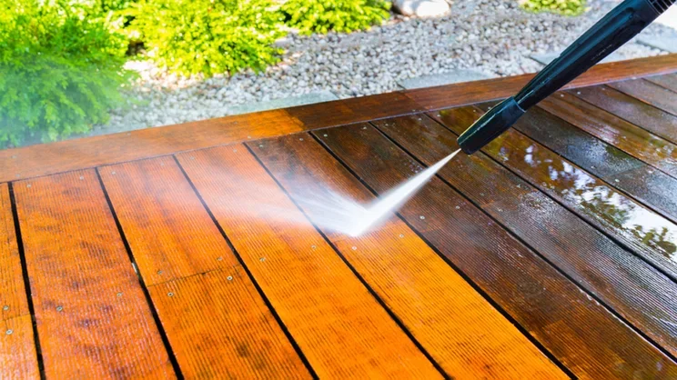 A power washer cleaning a wooden deck, spraying water on the surface.