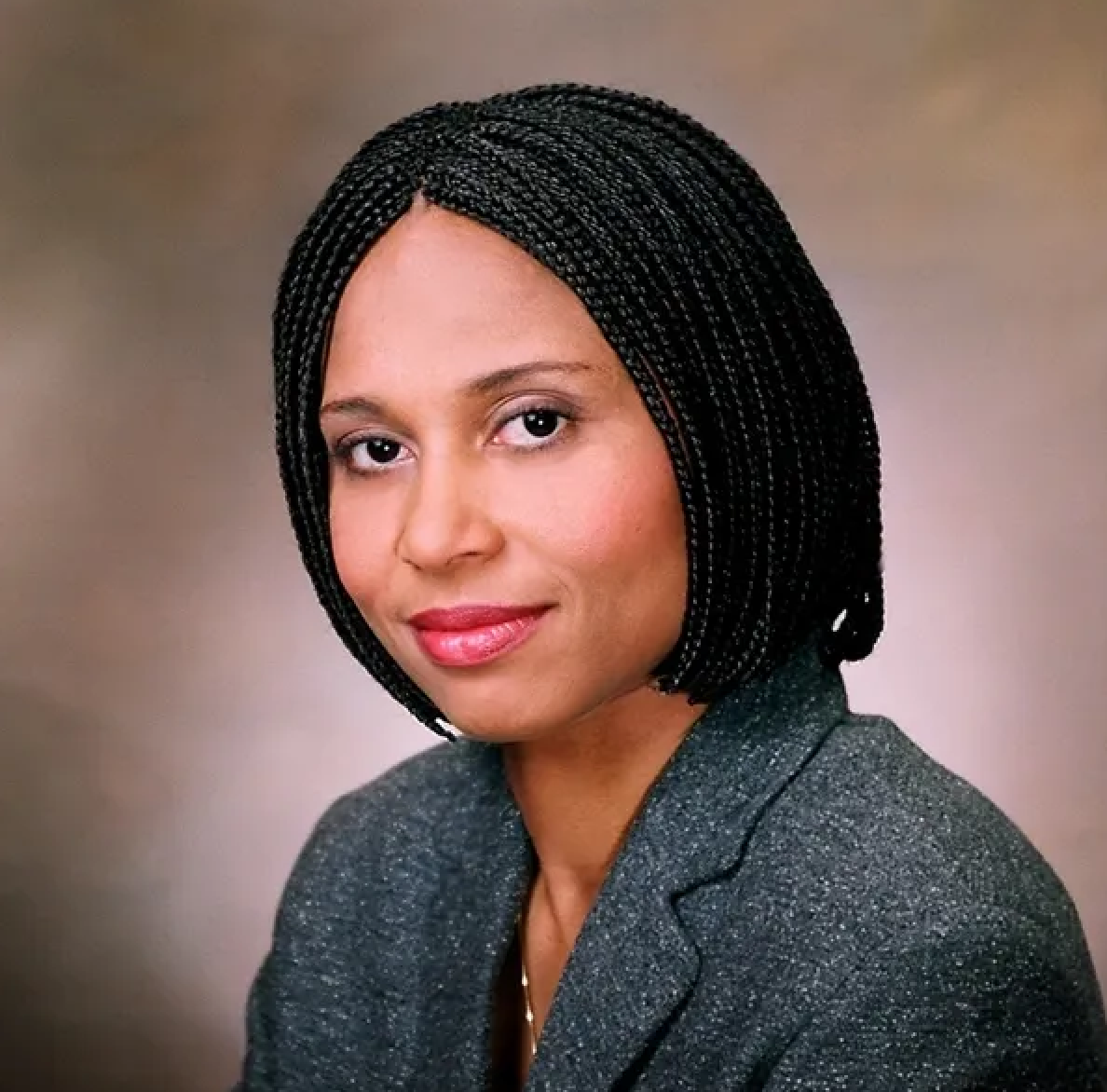 Professional woman with braided black hair, wearing a gray blazer, looking at the camera with a slight smile.