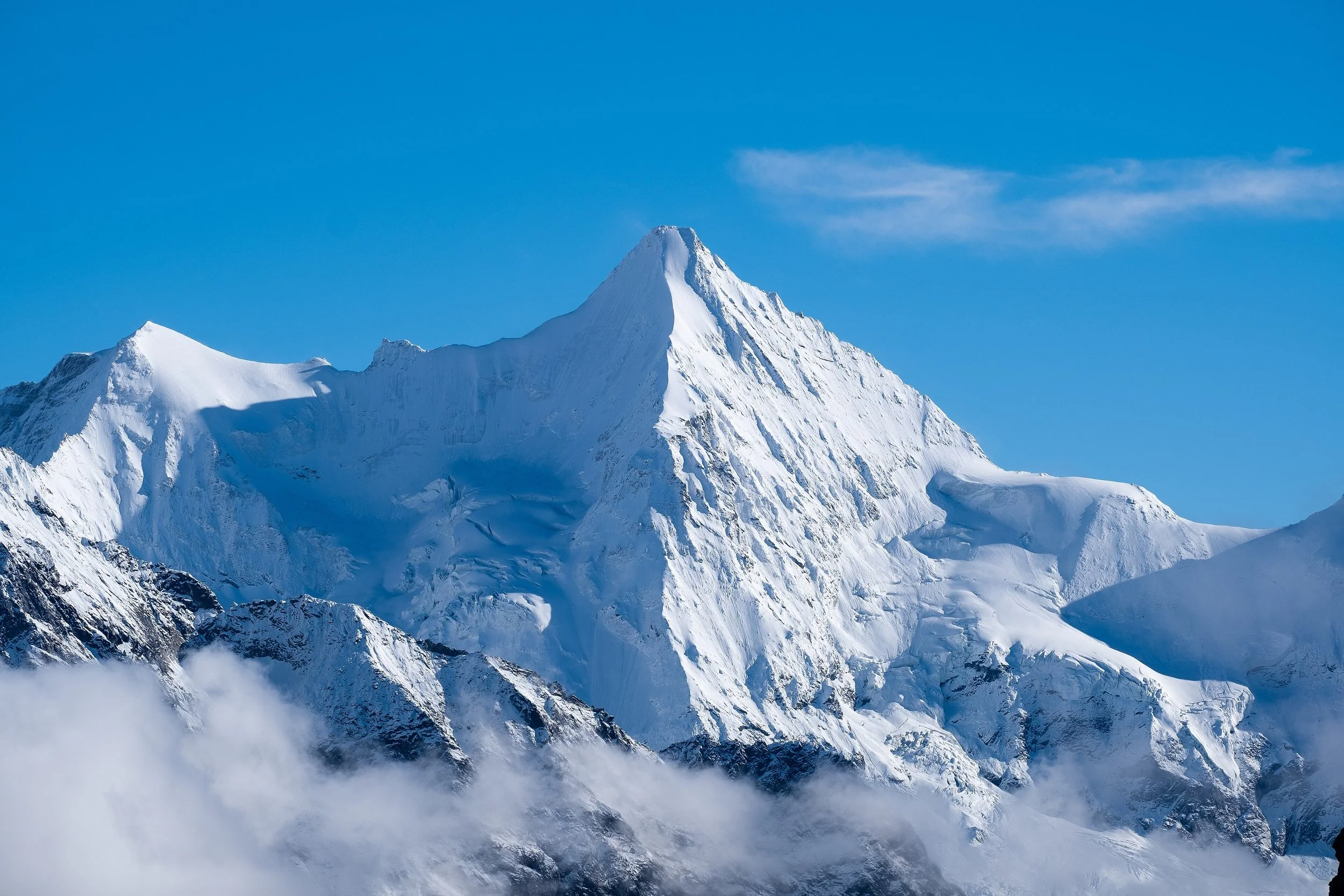 Montagne enneigée sous un ciel bleu avec quelques nuages légers.