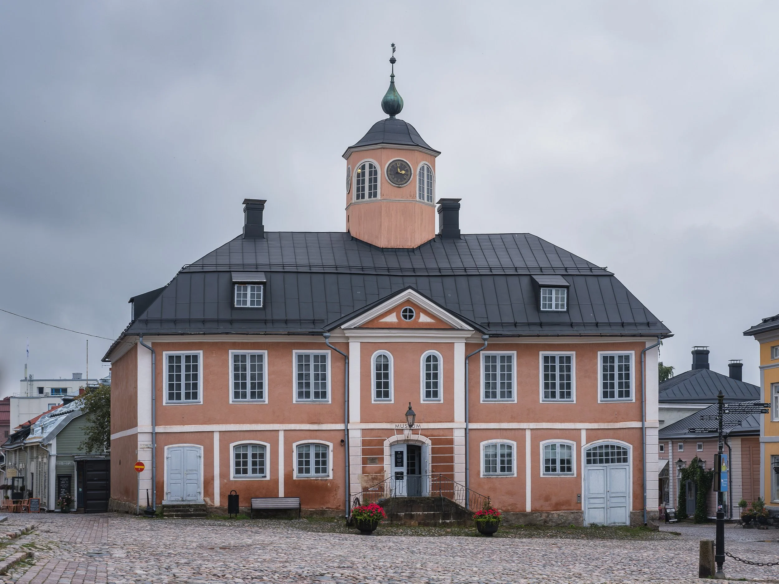 Une façade de bâtiment coloré avec une horloge au sommet et un drapeau norvégien. Près de l'entrée, il y a une affiche indiquant qu'il s'agit d'un musée.