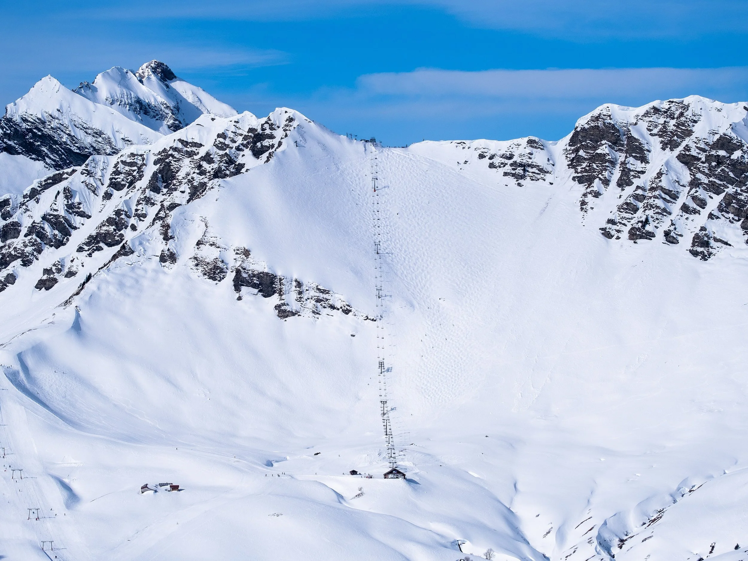 Montagnes enneigées avec des pistes de ski et des bâtiments au premier plan.