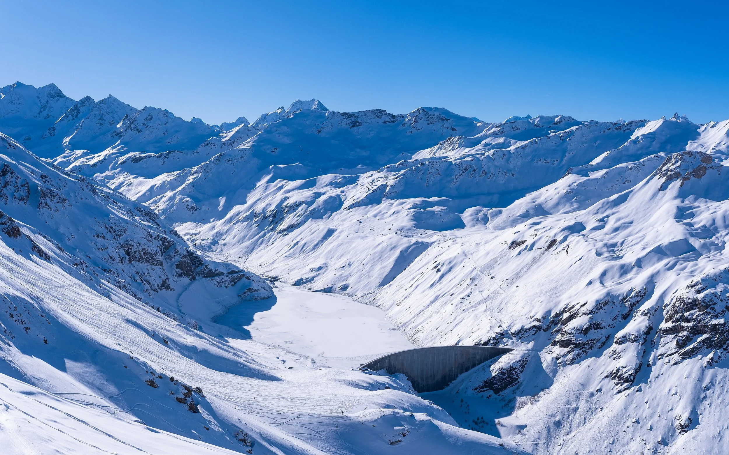 Chaîne de montagnes enneigées sous un ciel clair, avec un canyon au premier plan.