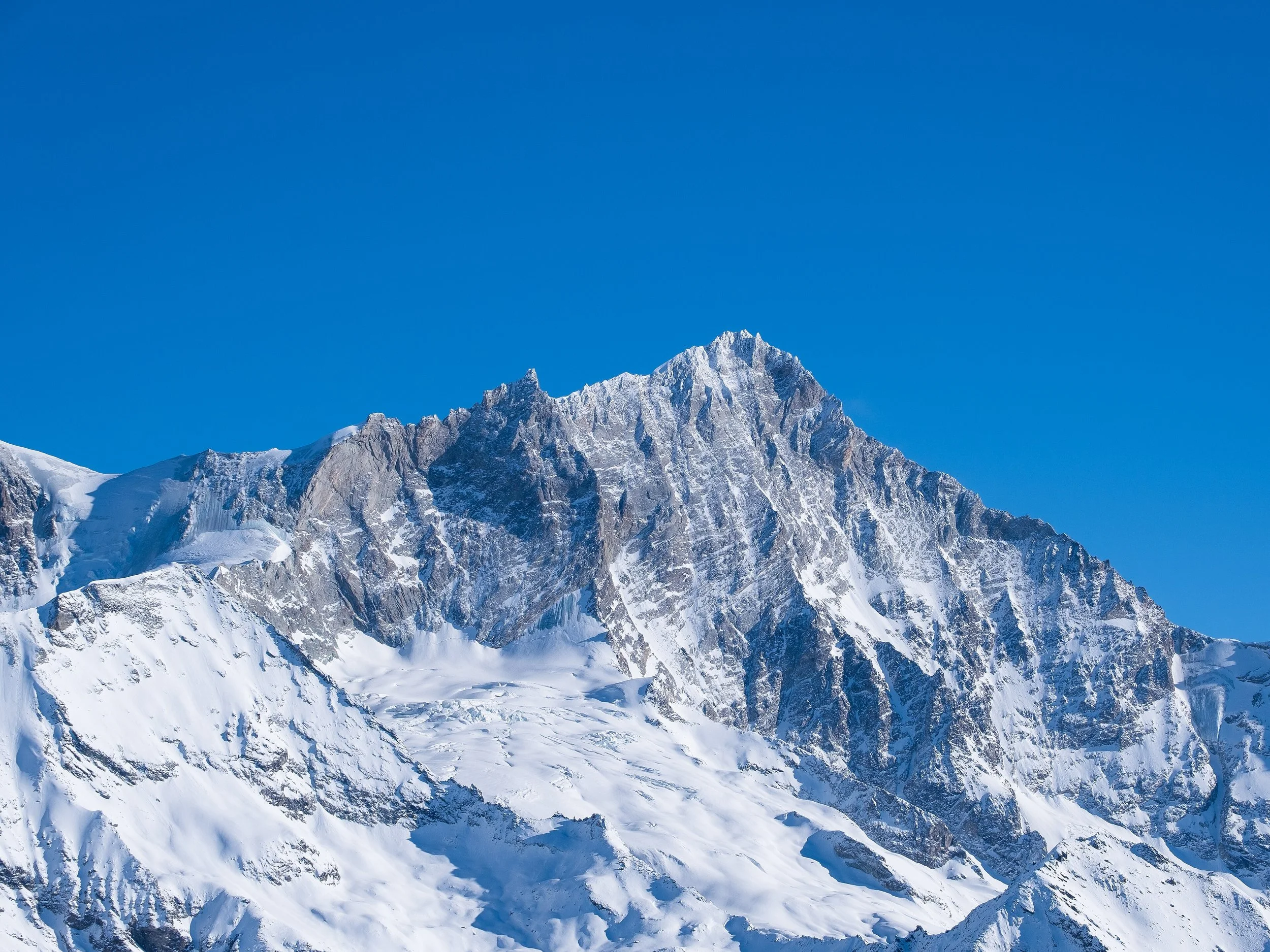 Montagne enneigée avec sommet rocheux et ciel bleu clair.
