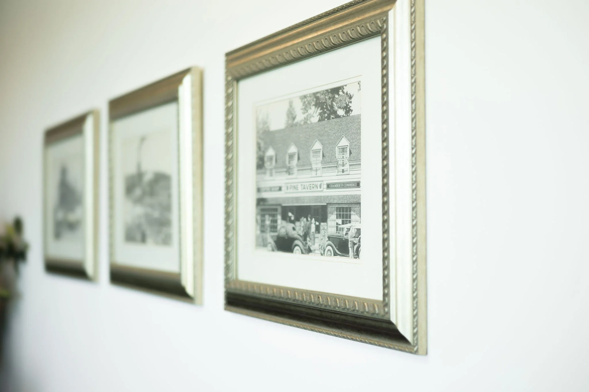 Photographs of vintage buildings and cars in frames on a white wall.