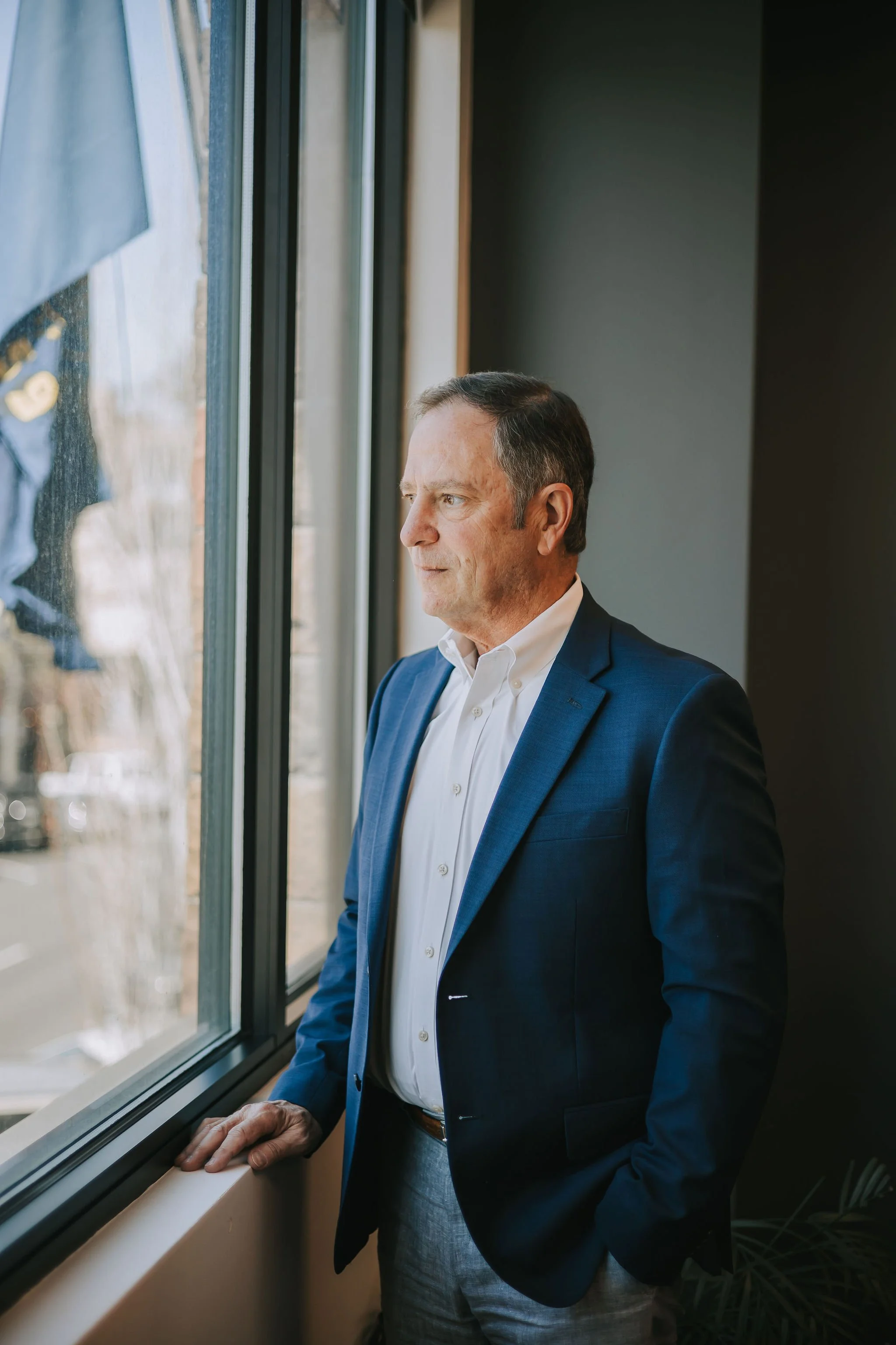 Jeff Klein of Klein Investment Strategies, financial investment firm located in Bend, Oregon in a blue suit looking out a window, standing near a windowsill, with natural light illuminating his face.