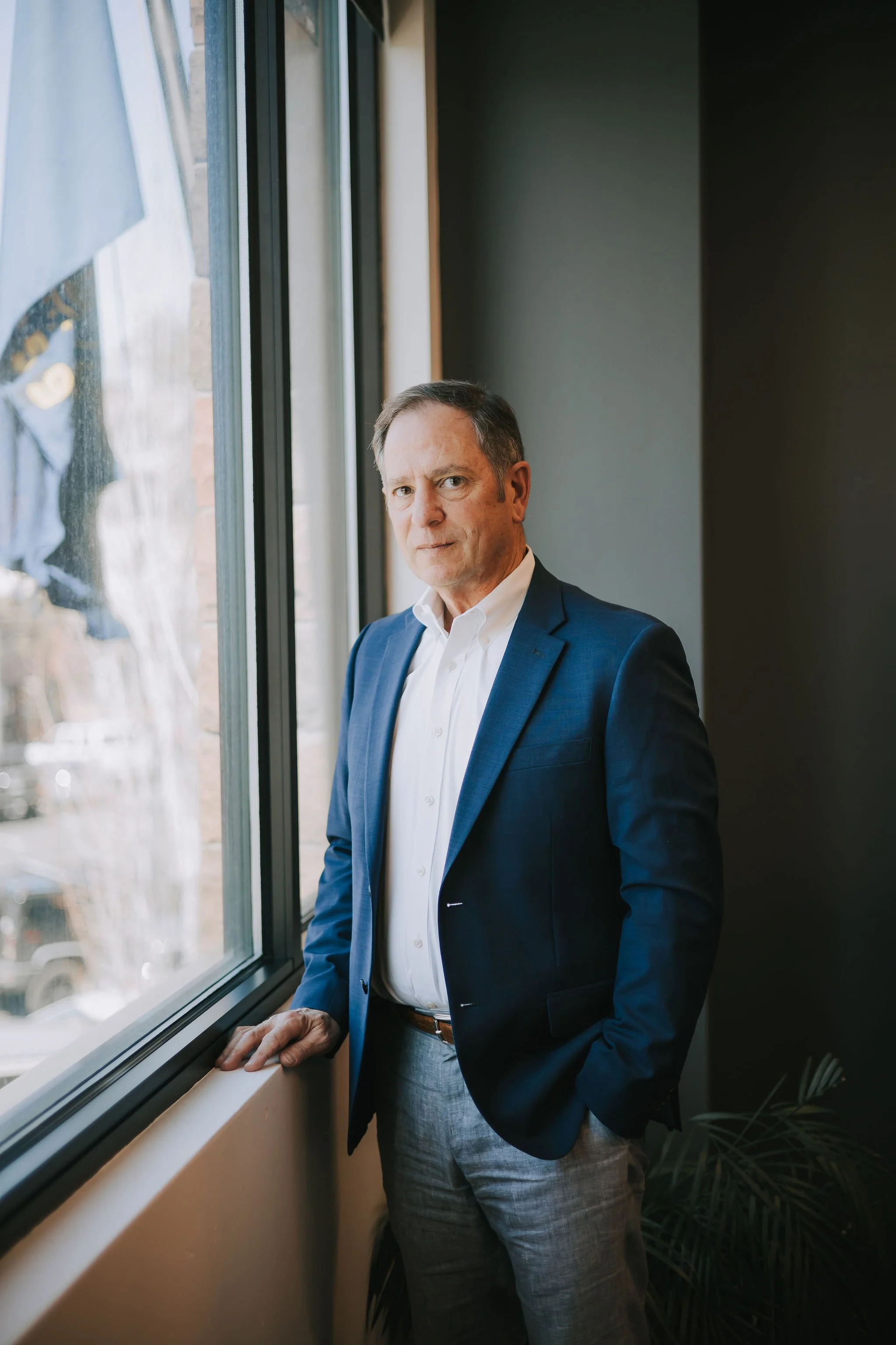 Jeff Klein of Klein Investment Strategies, financial investment firm located in Bend, Oregon in a blue suit looking out a window, standing near a windowsill, with natural light illuminating his face.