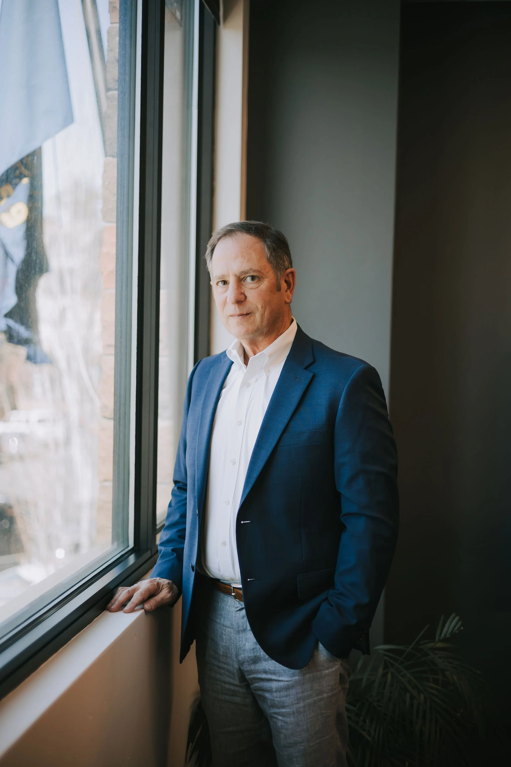 Jeff Klein of Klein Investment Strategies, financial investment firm located in Bend, Oregon in a blue suit looking out a window, standing near a windowsill, with natural light illuminating his face.