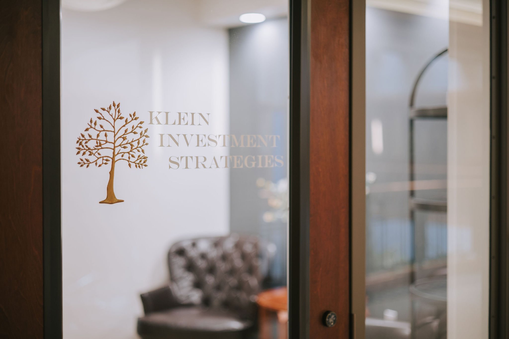 Interior view of an office or conference room through a glass door with "Klein Investment Strategies" logo and a tree symbol on it.