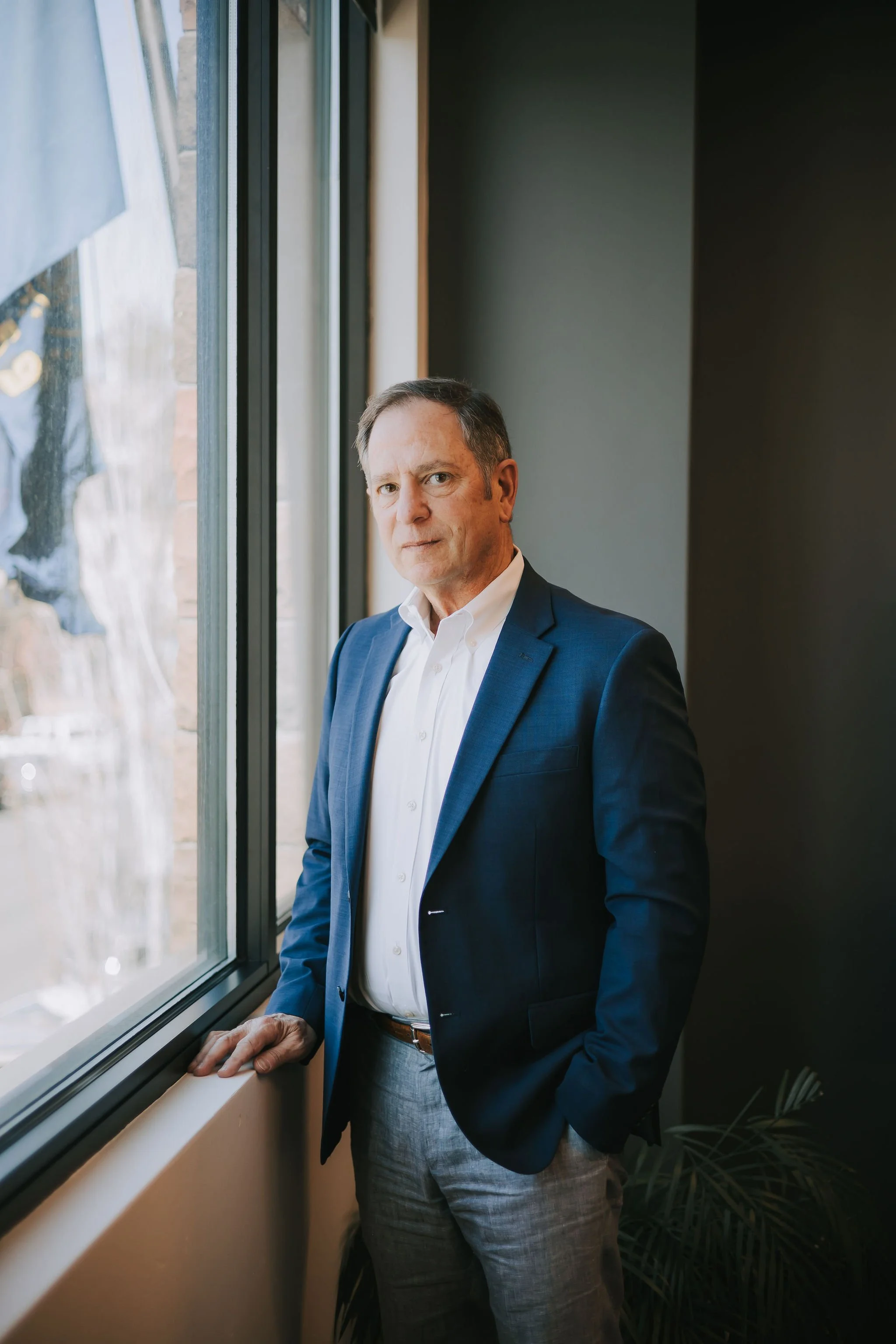 Jeff Klein of Klein Investment Strategies, financial investment firm located in Bend, Oregon in a blue suit looking out a window, standing near a windowsill, with natural light illuminating his face.