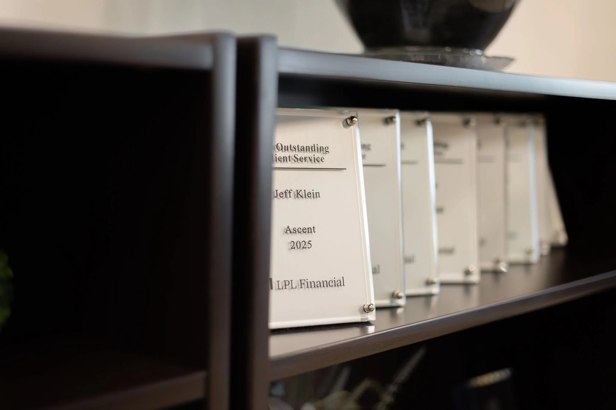 Shelf with binders labeled 'Outstanding Client Service' and names including Jeff Klein, related to an ascent in 2025, in an office setting.