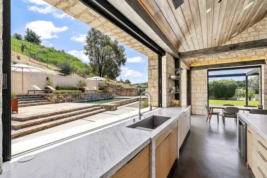Modern kitchen with open view of an outdoor pool area and landscaped yard.