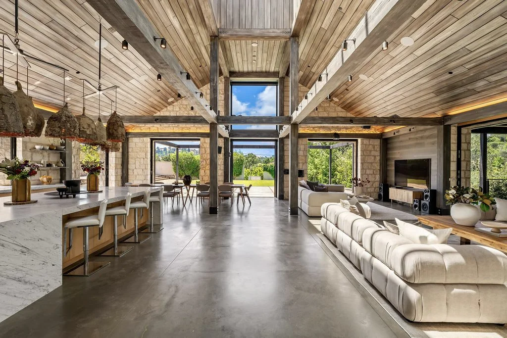 Open-concept modern living room and kitchen with high vaulted wooden ceiling, large windows, and minimalistic decor.