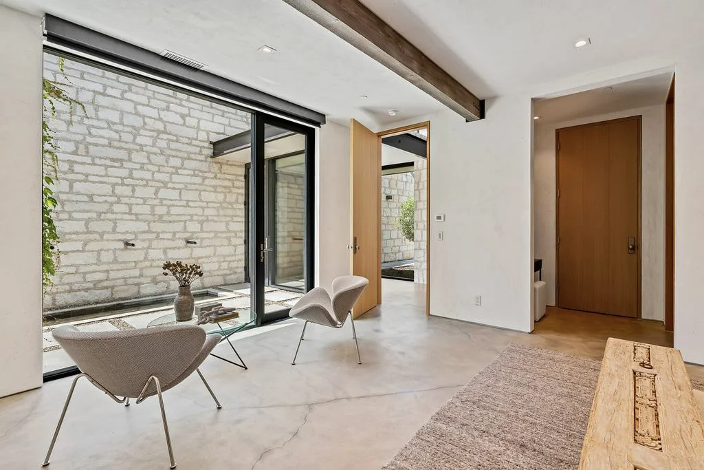 Minimalist living room with large glass sliding doors, modern chairs, a glass coffee table, and a stone wall outside.