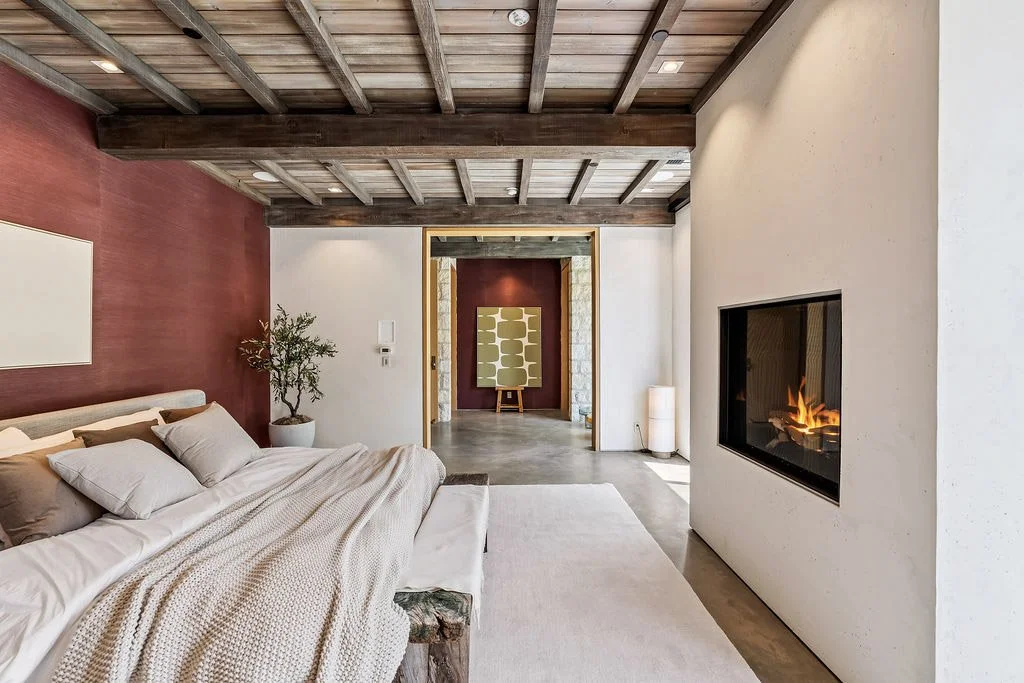 Modern bedroom with a large bed, wood ceiling, fireplace, potted plant, and artwork on the wall.