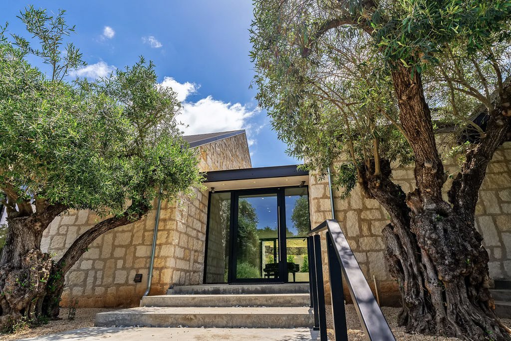 Stone building with glass door, trees on each side, and steps leading up to the entrance, under a partly cloudy blue sky.
