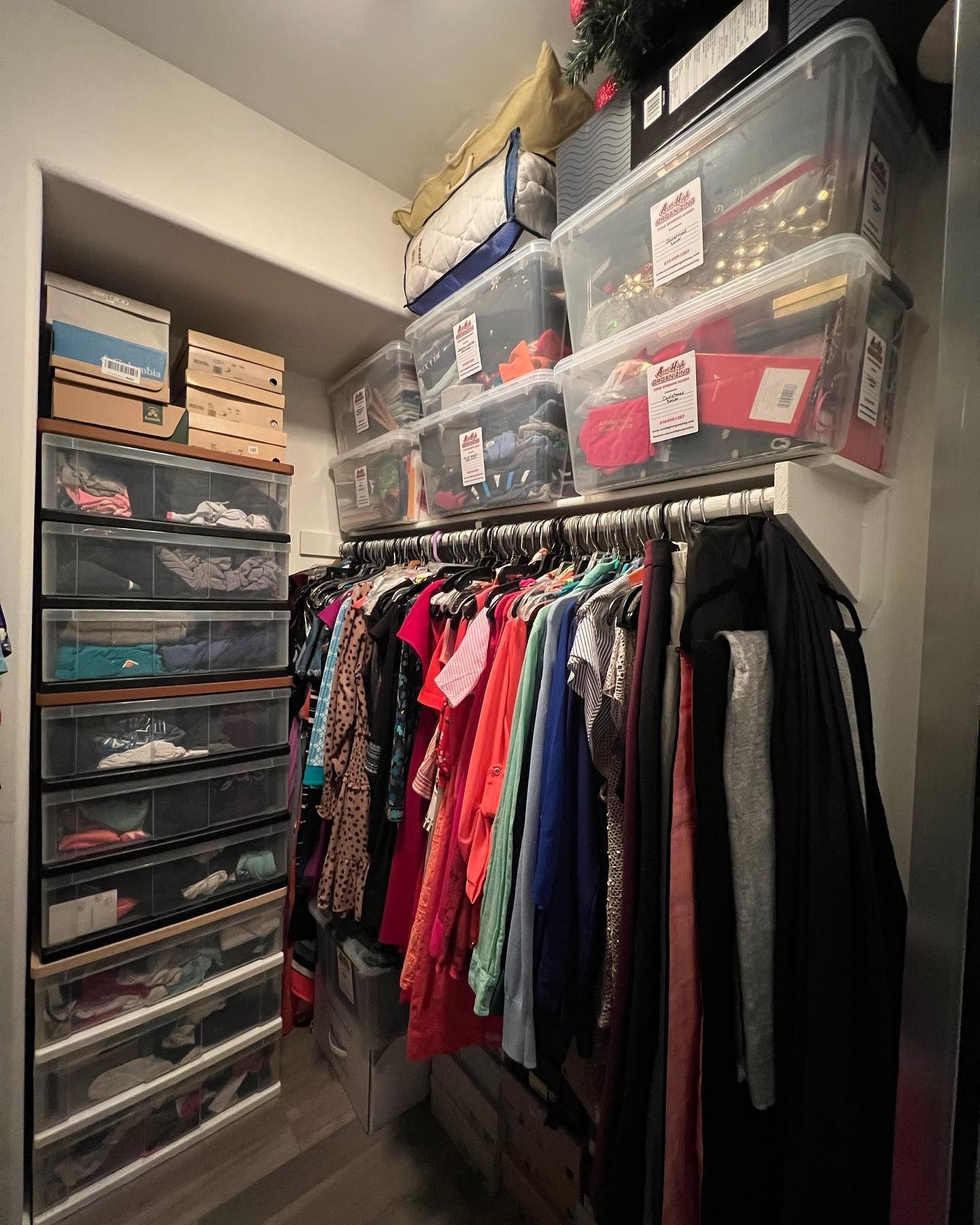 Closet with multiple storage bins and drawers filled with clothes, and a clothing rack with various colorful garments hanging.