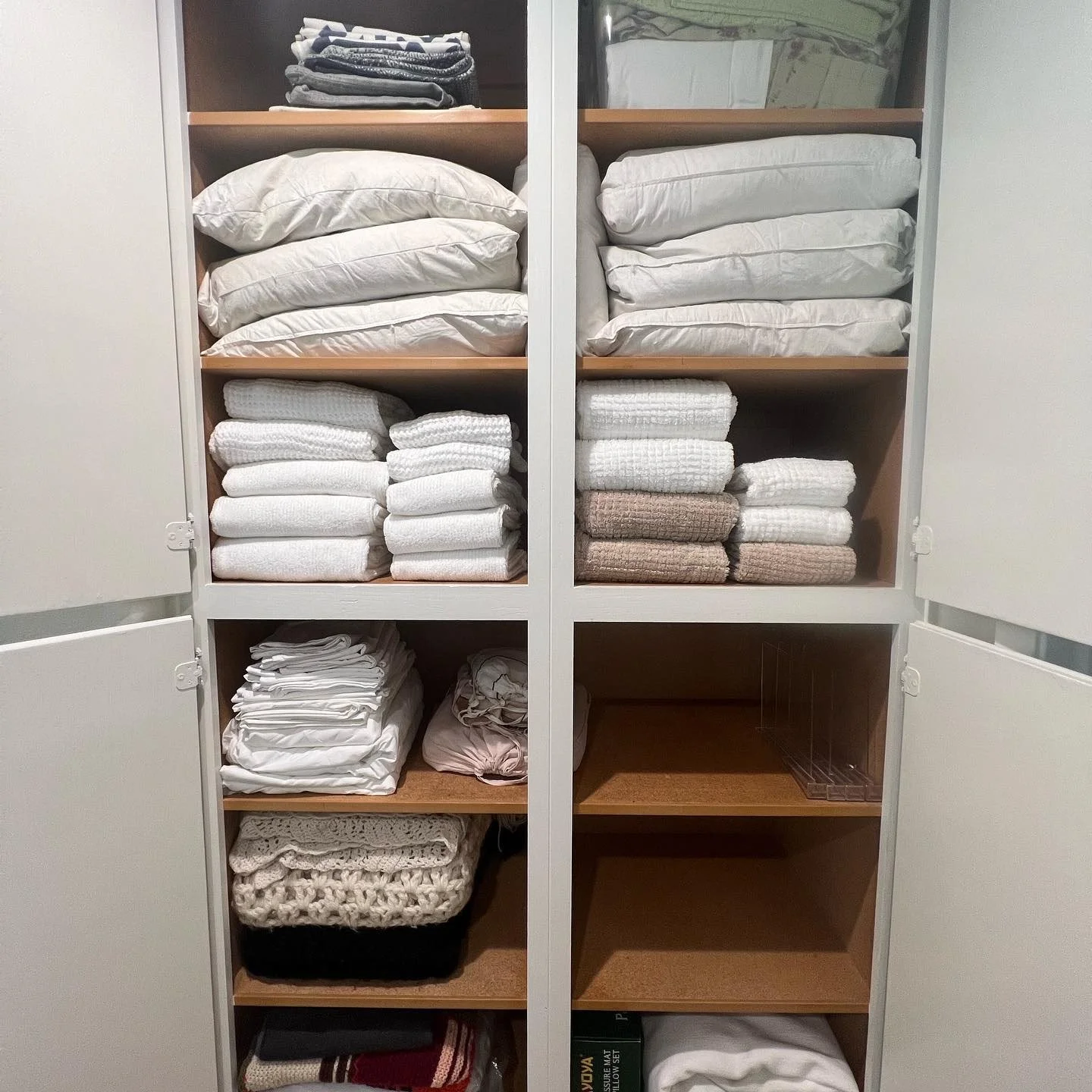 Shelves of folded linens, towels, and blankets inside a white cabinet