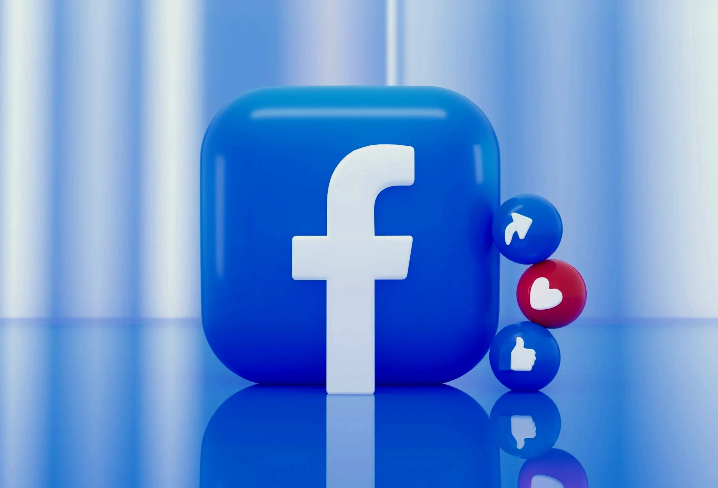 Close-up of a blue Facebook logo icon with smaller notification icons showing a thumbs-up, a heart, and a comment bubble, reflecting on a shiny surface.