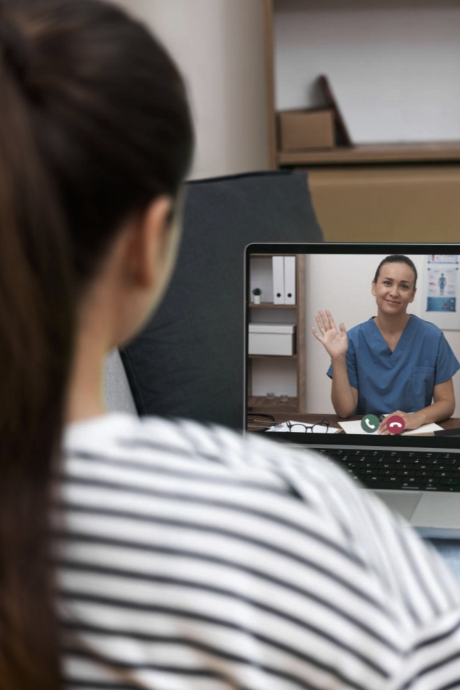 A woman with long dark hair in a ponytail wearing a white and black striped shirt is on a video call with a person dressed as a nurse in blue scrubs, who is waving.