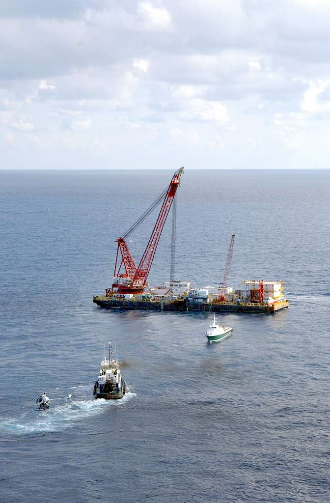 A large barge with a red crane and equipment on the water, accompanied by smaller boats.
