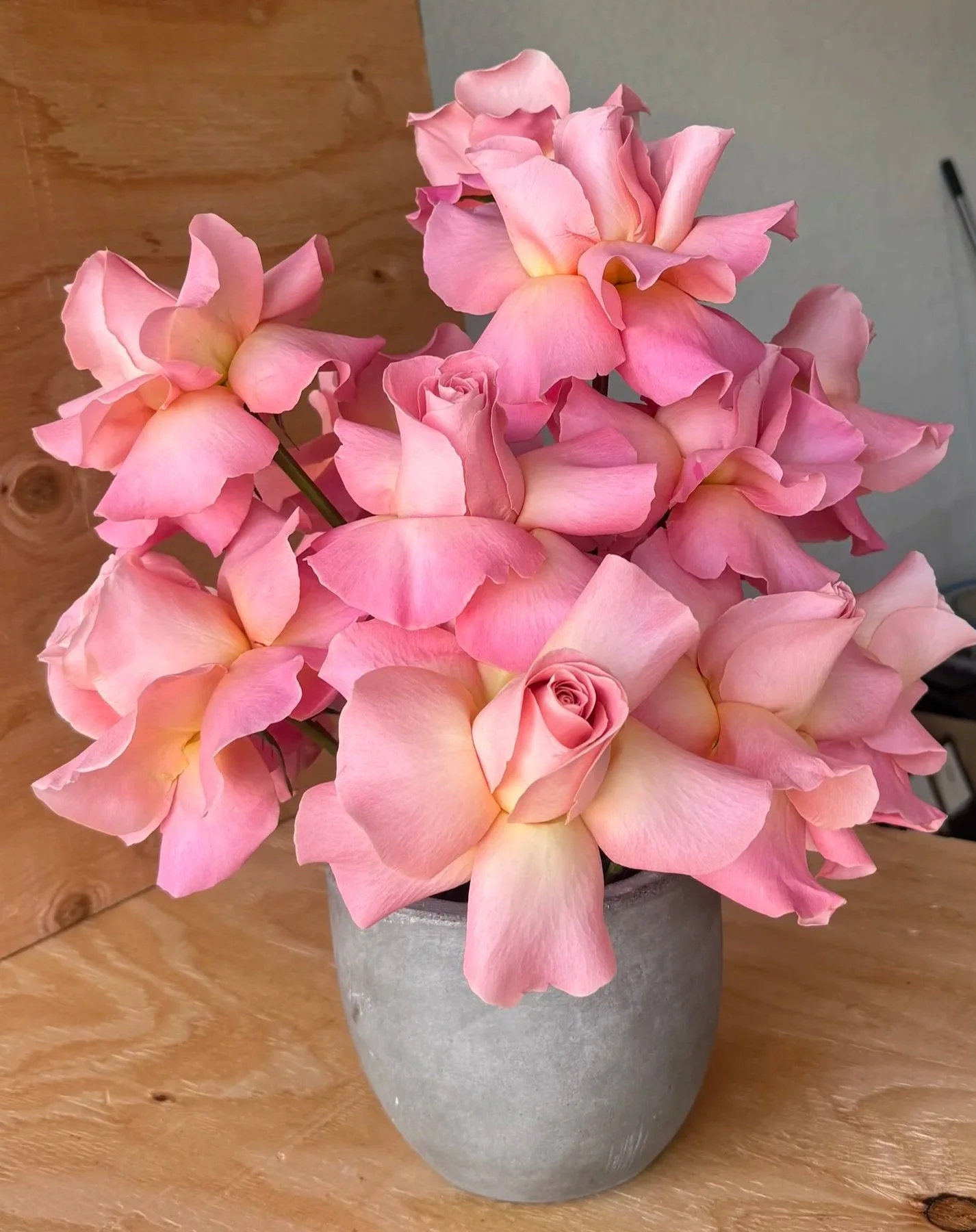 A flower arrangement of pink roses and pink hydrangeas in a gray vase on a wooden surface.