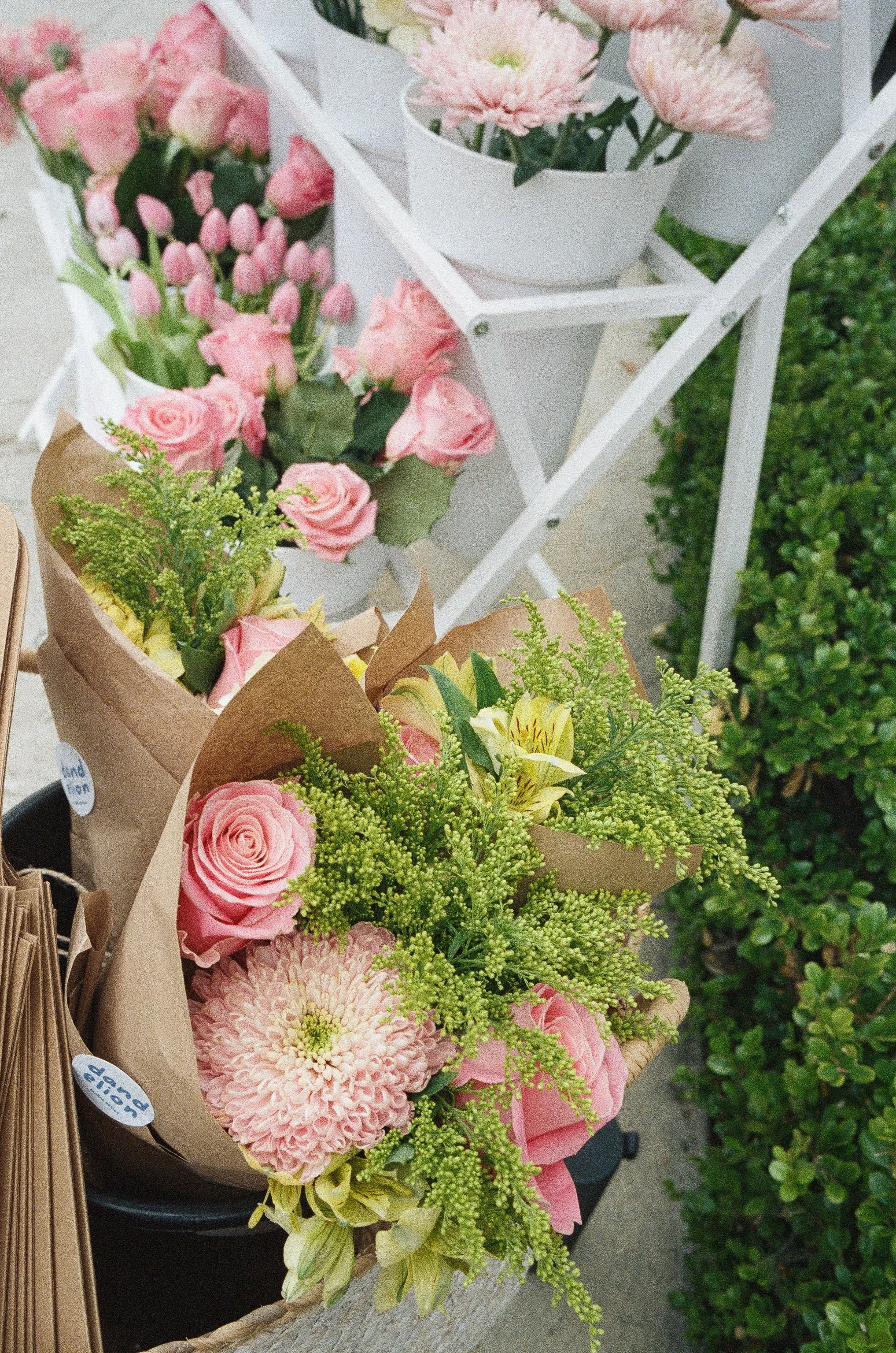 Pink and white flower bouquets on display with a white shelving unit and greenery in the background.