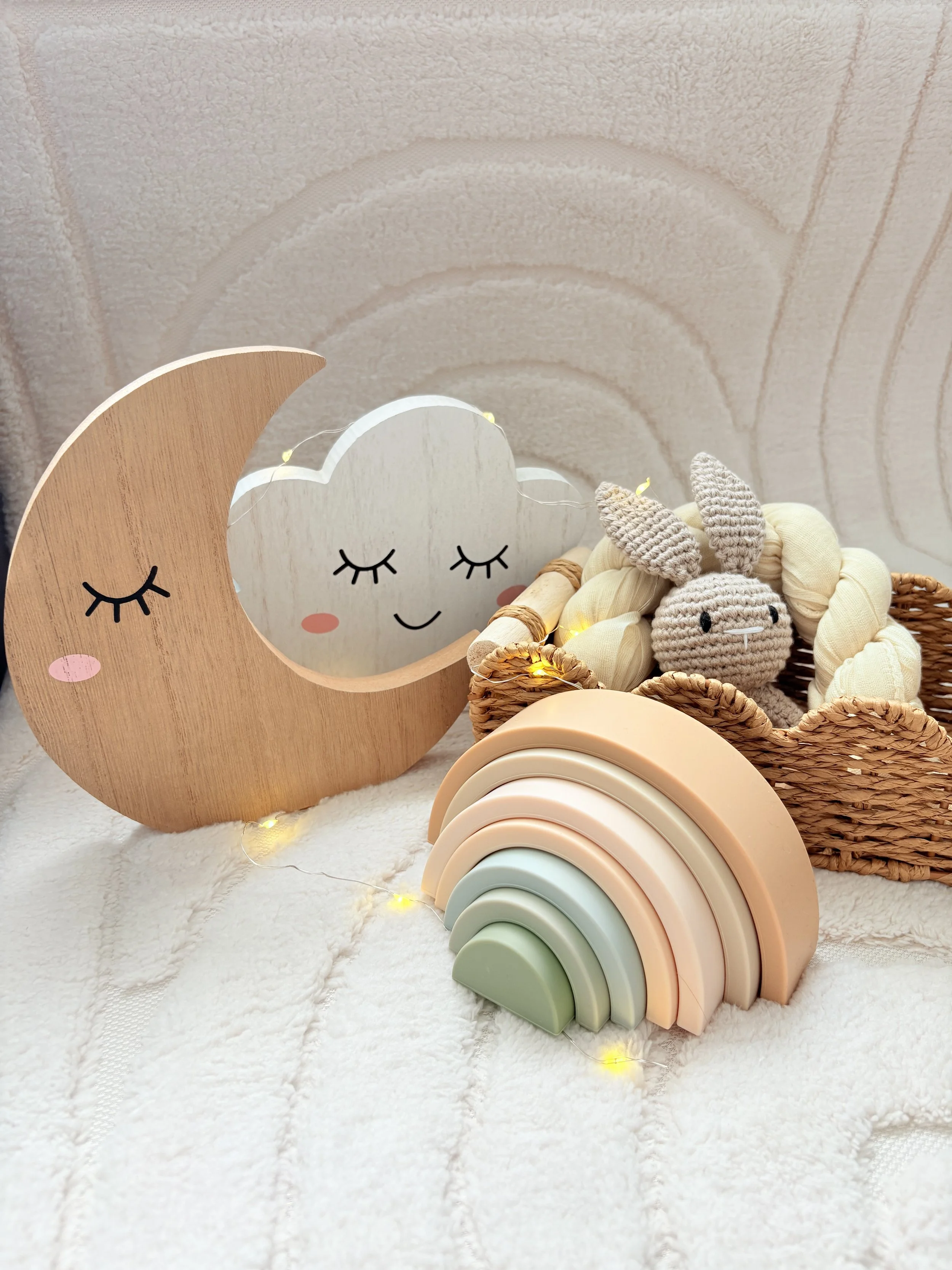 Sensory play setup for The Wonder Collective, featuring wooden moon and cloud characters, a pastel wooden rainbow, soft toys and warm fairy lights.