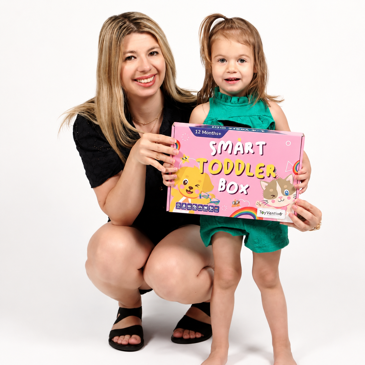 Mulher com cabelo loiro e menina com cabelo castanho claro, ambos sorrindo e segurando caixa de brinquedos chamada "Smart Toddler Box", em fundo branco.